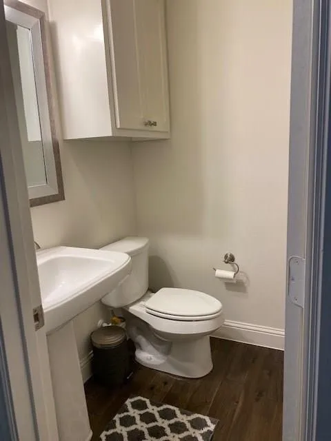 Pedestal sink, wall-mounted white cabinetry, wood-finish flooring, and white baseboards