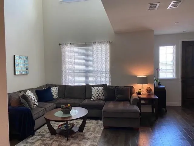 Vaulted ceiling, dark wood-finish flooring, two windows with blinds, and a dark wood door