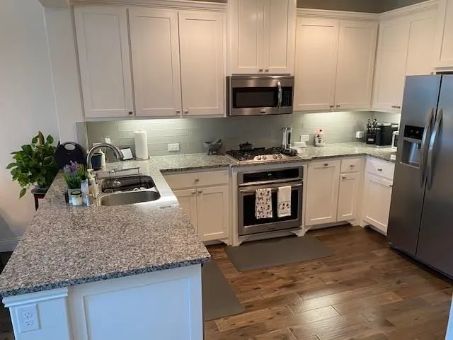 Kitchen featuring white cabinetry, stainless steel appliances, granite countertops, a tile backsplash, and wood-finish flooring