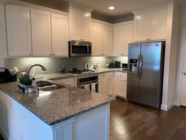 White cabinetry with crown molding, stainless steel appliances, granite countertops, tile backsplash, and wood-finish flooring