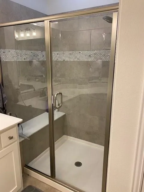 Glass-enclosed shower with brushed nickel hardware, tiled walls, decorative mosaic tile band, and a built-in shower bench