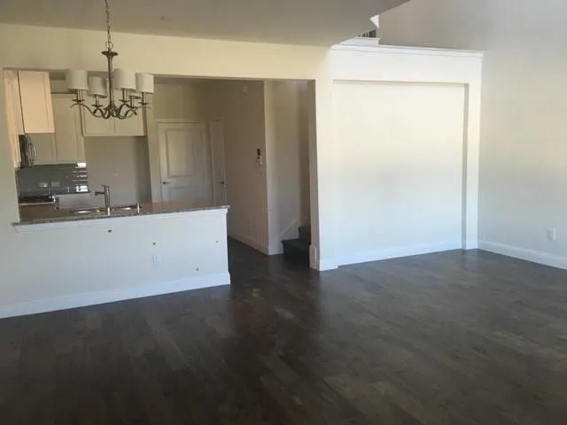 Open concept living area featuring dark wood-finish flooring, a kitchen with white cabinetry, a granite-style countertop, and a built-in stainless steel sink with a gooseneck faucet