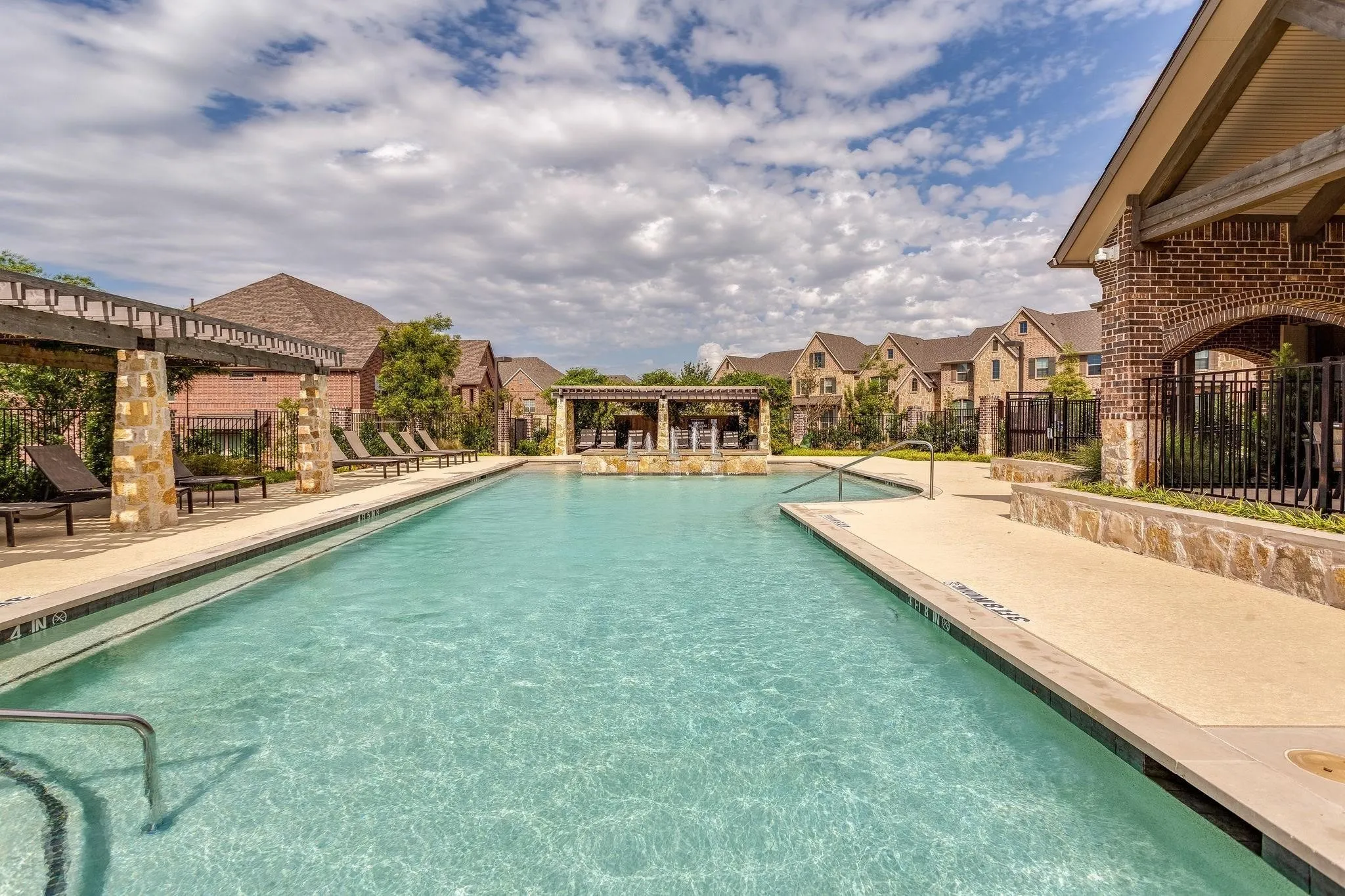 Community swimming pool featuring a tanning ledge, perimeter concrete decking, and stone-clad pergolas