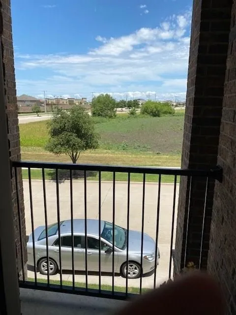 Balcony featuring a black metal railing, brick pillars, and a distant treeline