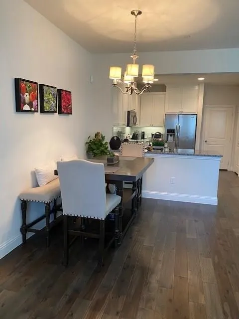 Open-concept kitchen and dining area featuring a wood-finish plank floor, stainless steel appliances, white cabinetry with a large island, and a coordinating dining table space