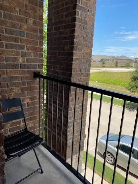 Balcony featuring a concrete floor, dark brick walls, and a black metal railing