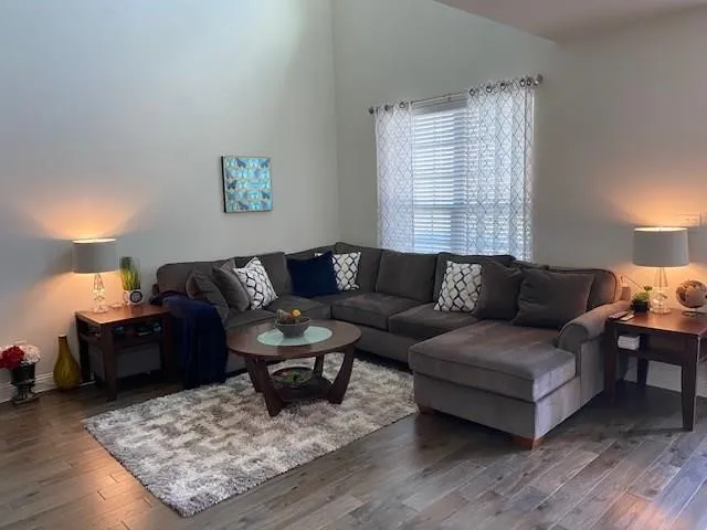 Vaulted ceiling, wood-finish flooring, rectangular window with blinds, light gray walls