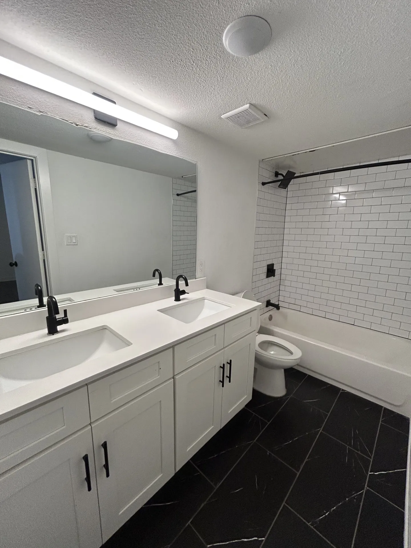 Dual vanity with integrated sinks, white cabinetry, black hardware, black tile flooring, and subway tile shower surround with black fixtures