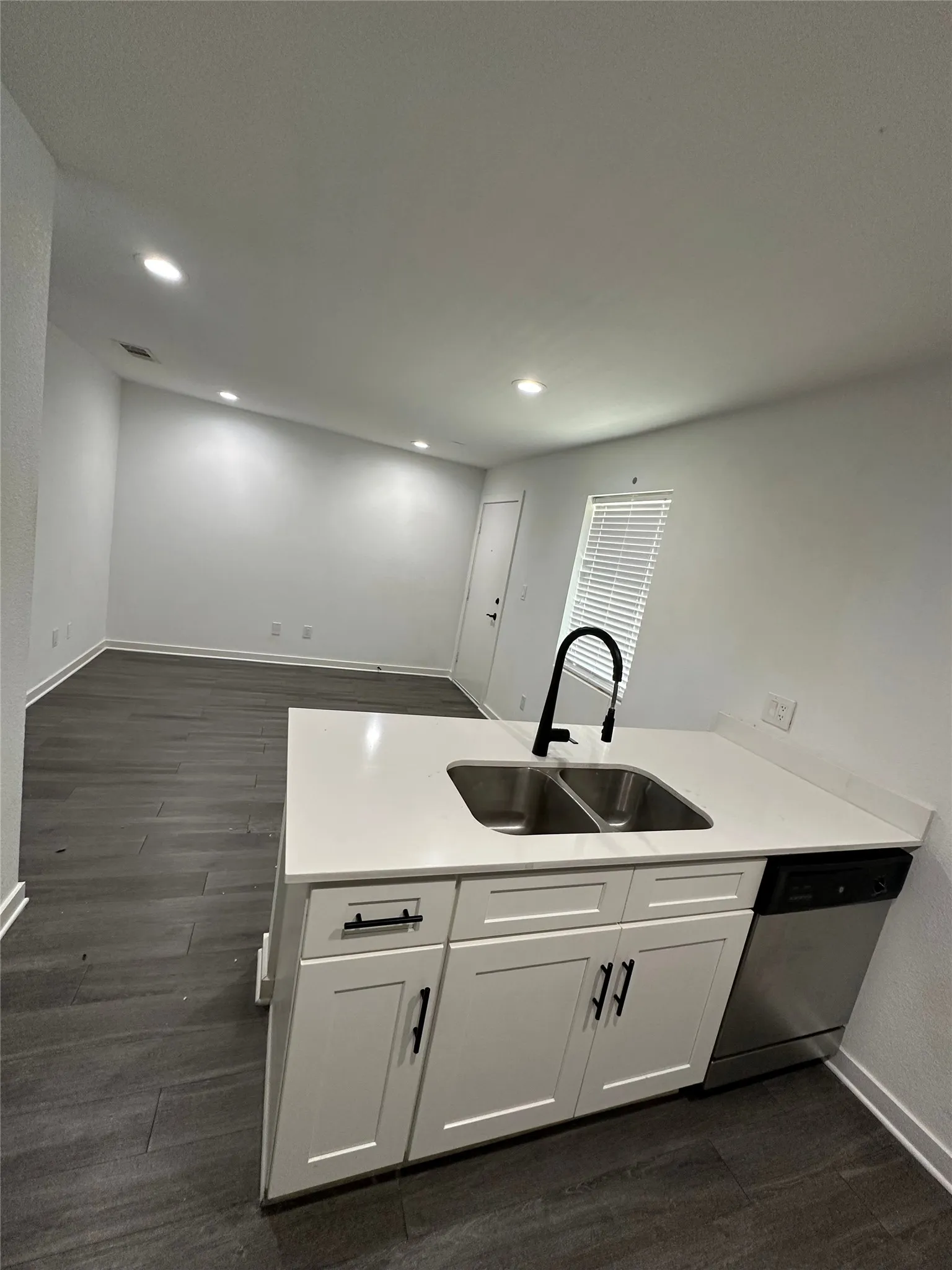 Kitchen island with white shaker cabinetry, stainless steel double basin sink, white countertops, and integrated dishwasher