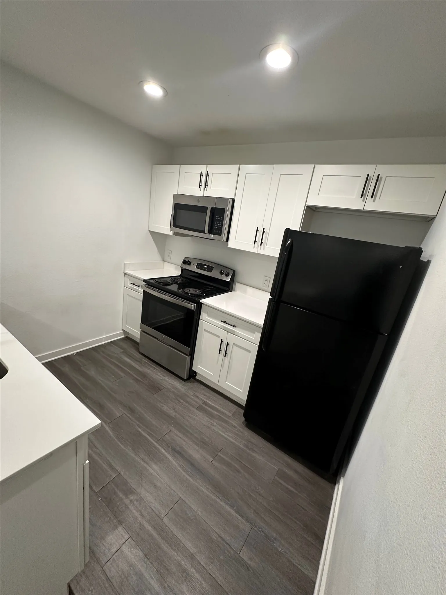 Modern kitchen featuring white cabinetry, light countertops, stainless steel microwave and range, and wood-finish flooring