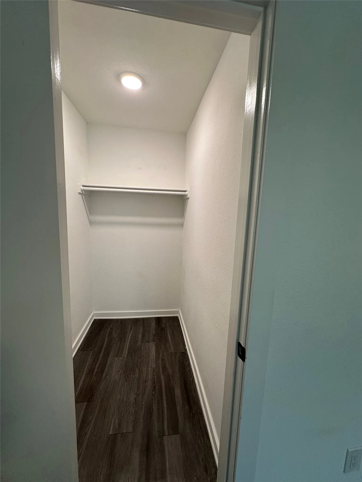 Dedicated walk-in closet featuring white walls, recessed ceiling lighting, built-in shelving, and dark wood-finish flooring