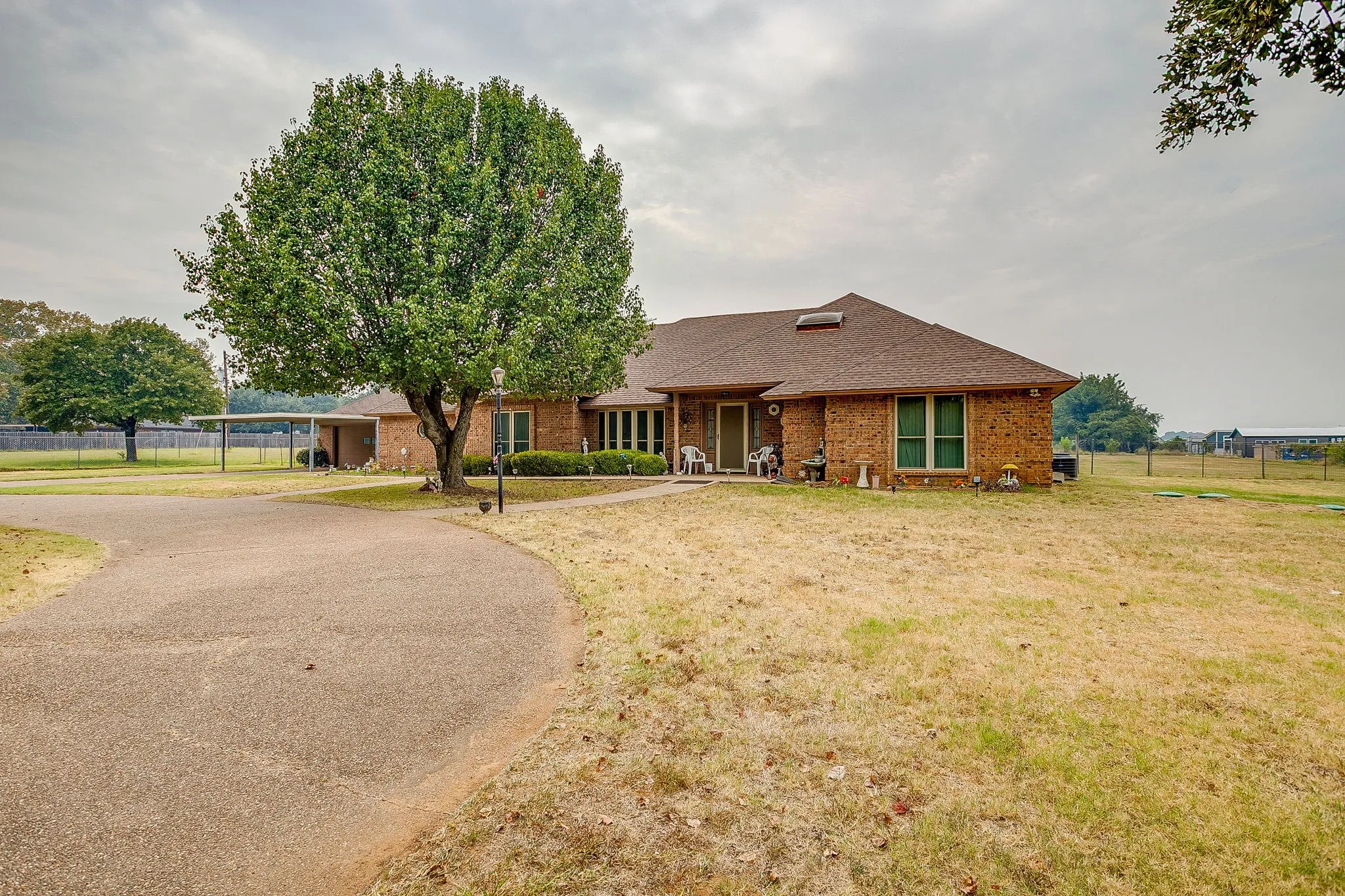 Brick exterior, mature front yard tree, curved paved driveway, attached carport, and covered front entry