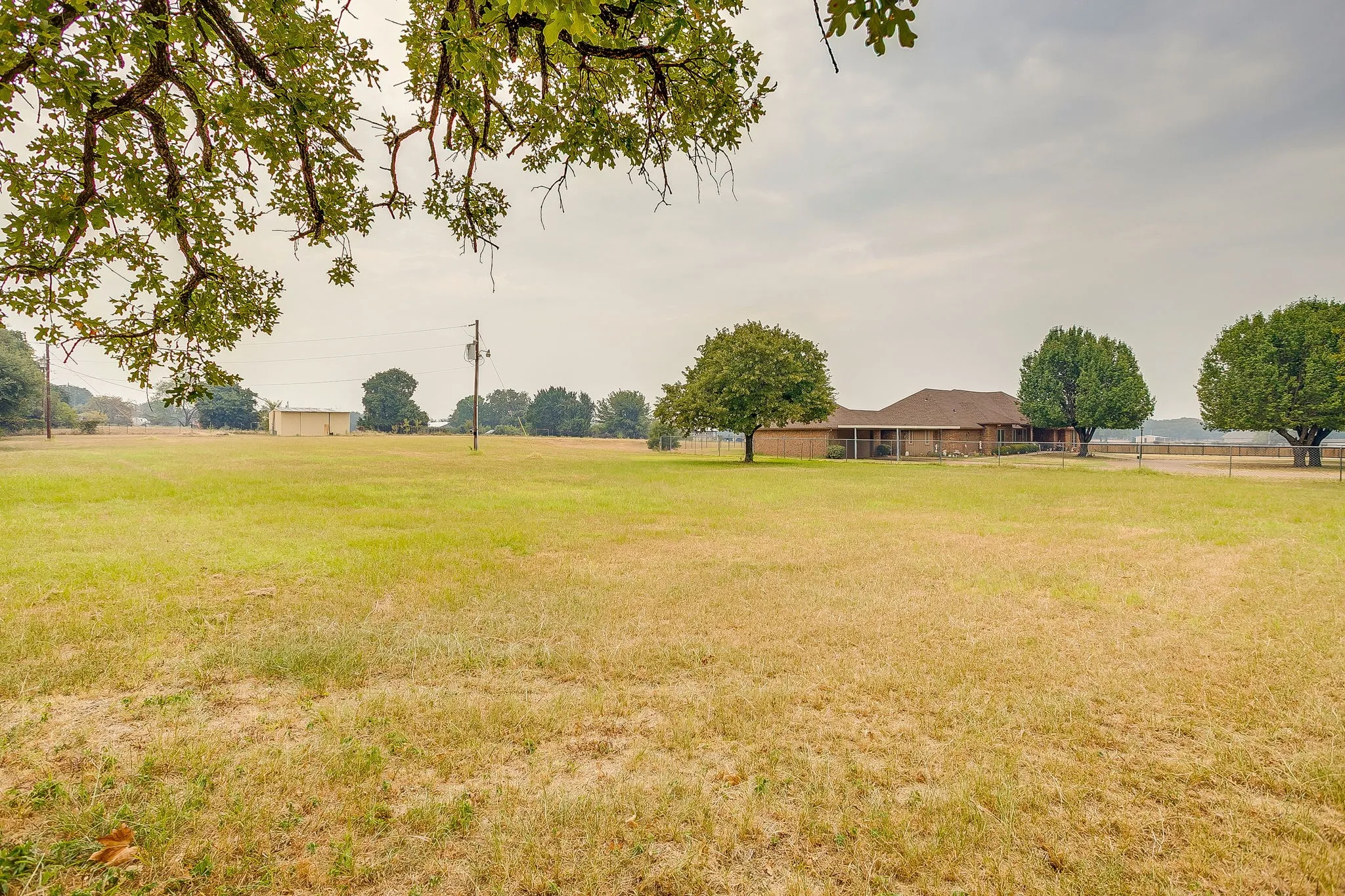 Expansive green space featuring scattered mature trees and a single-story residence with a brown roof