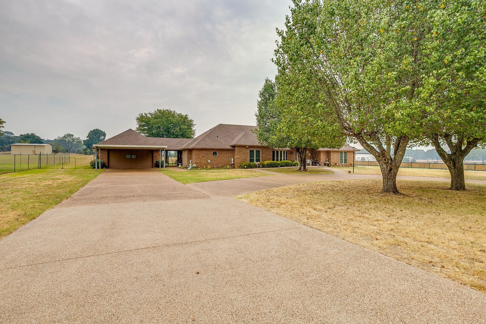 Brick exterior residence with a covered carport, mature trees, and a spacious driveway