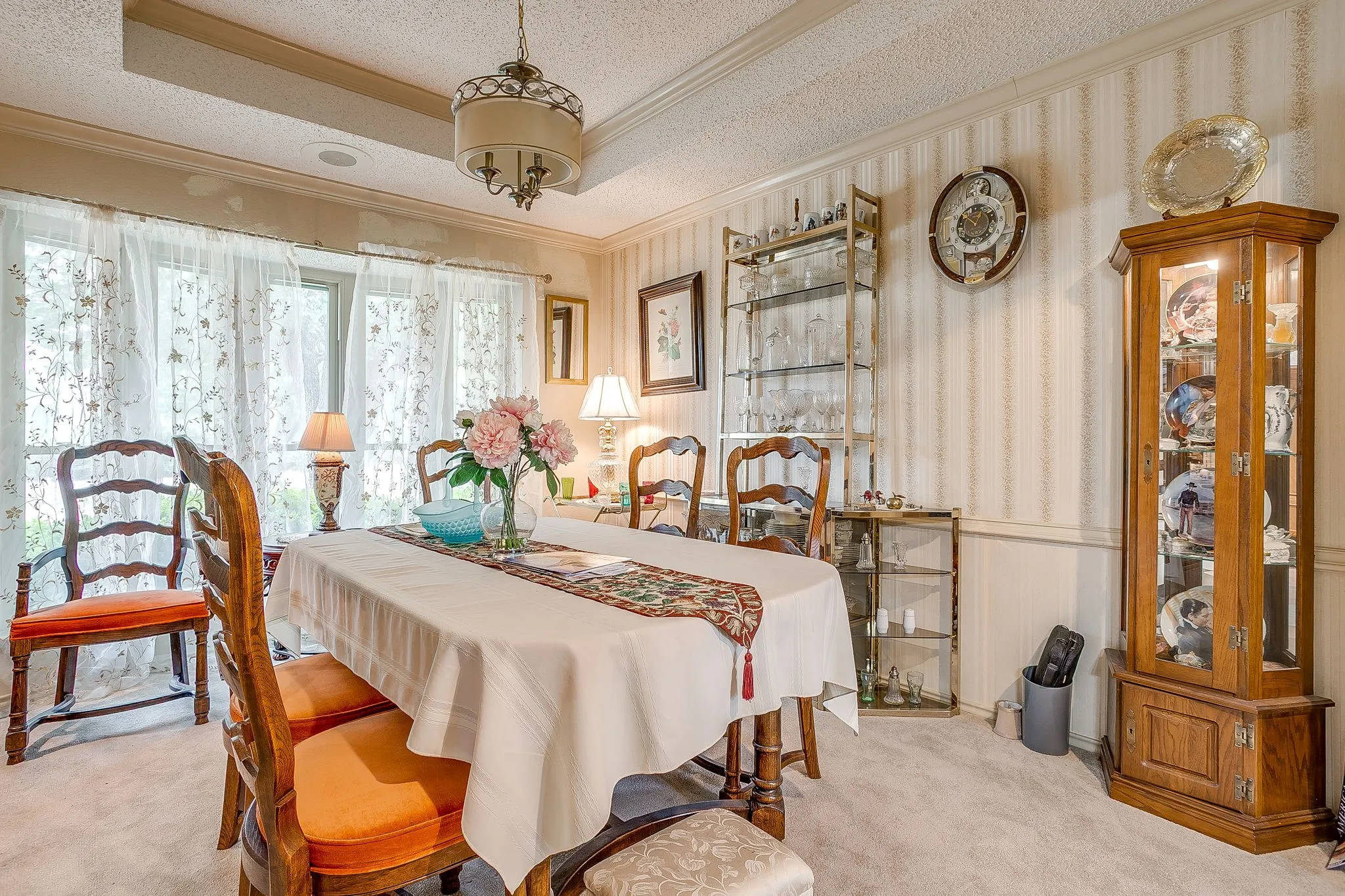 Recessed ceiling beam, decorative chandelier, large window with sheer curtains, chair rail molding, and striped wallpaper