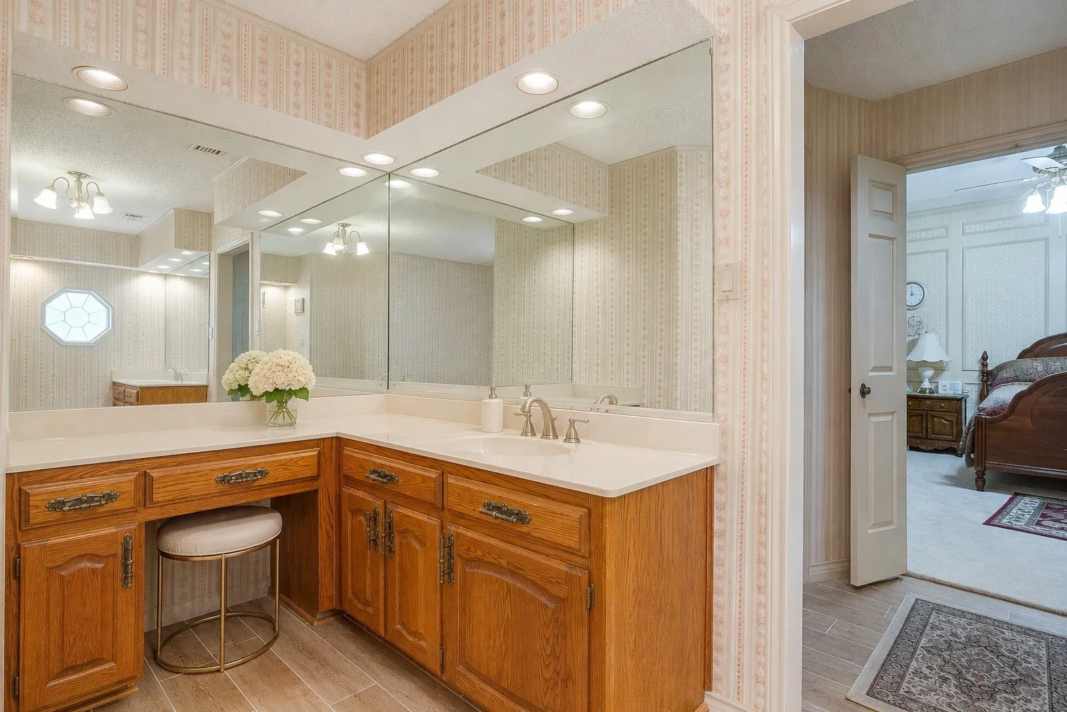 Expansive vanity counter with a built-in sink, wood-finish cabinetry, and full-wall mirrors (virtually edited)