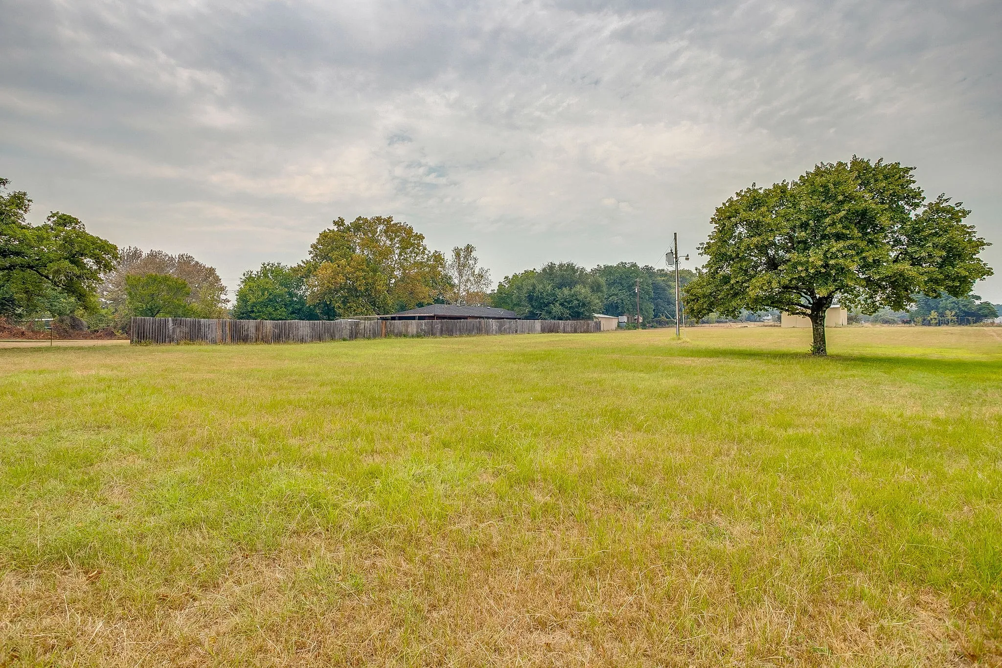 Expansive grassy terrain with mature trees and a perimeter fence