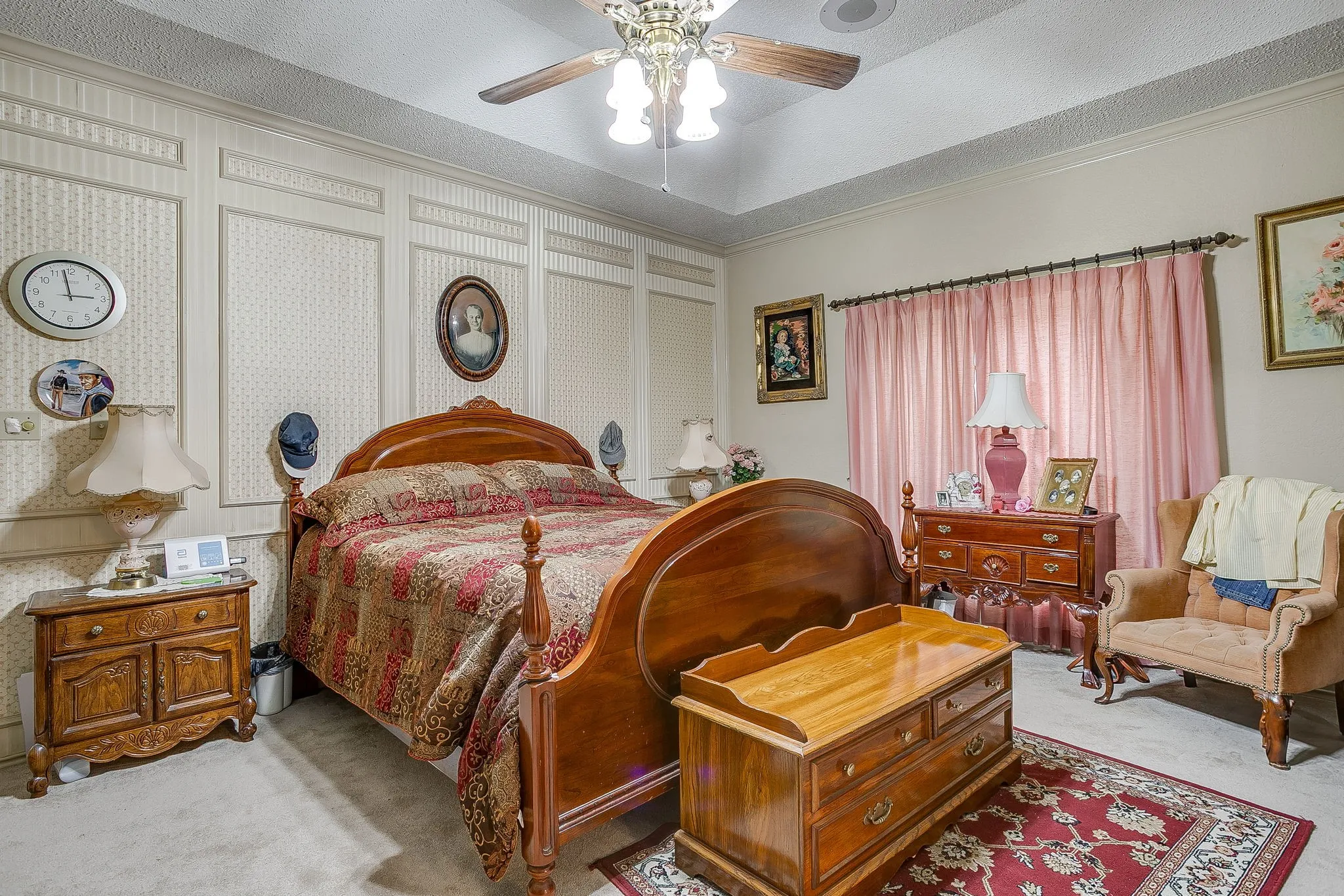 Tray ceiling with crown molding, patterned wallpaper with paneling, wood-finish ceiling fan, and carpeted flooring