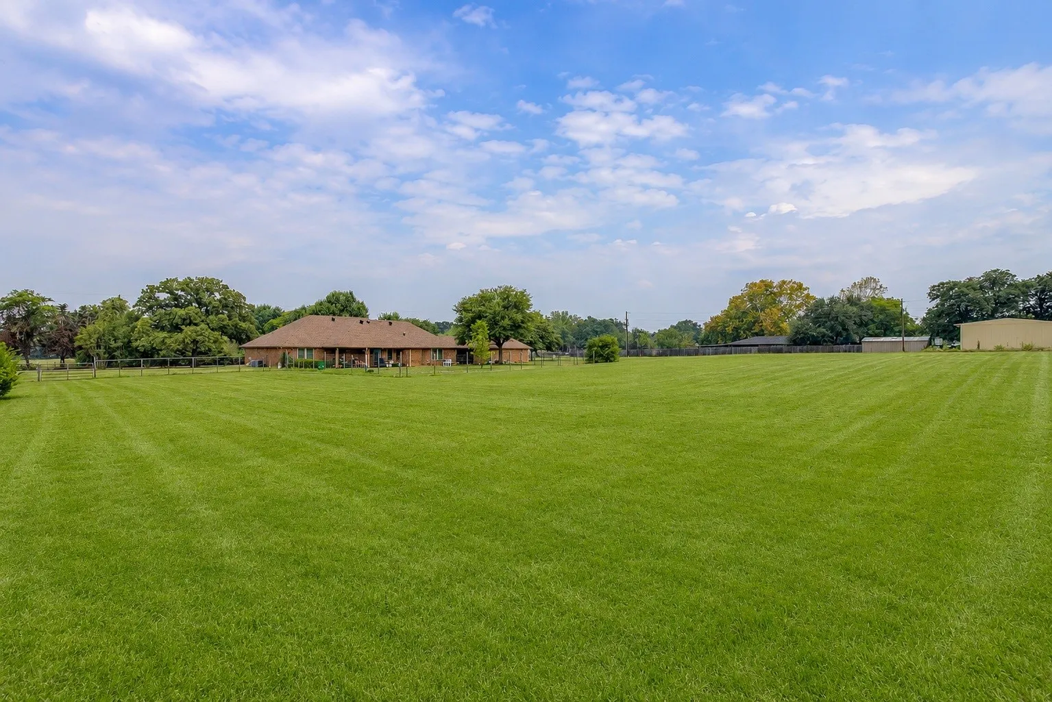 Expansive green lawn with mature trees and a single-story residence (added blued sky and greened grass)