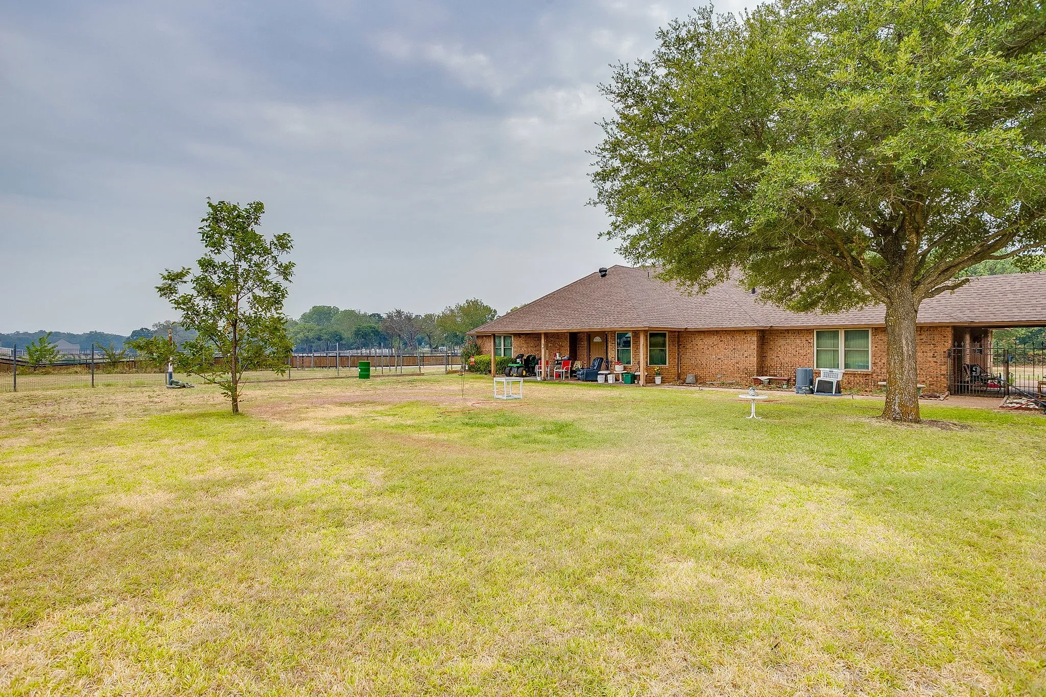 Expansive backyard featuring a mature tree, brick exterior, covered patio, and fenced perimeter