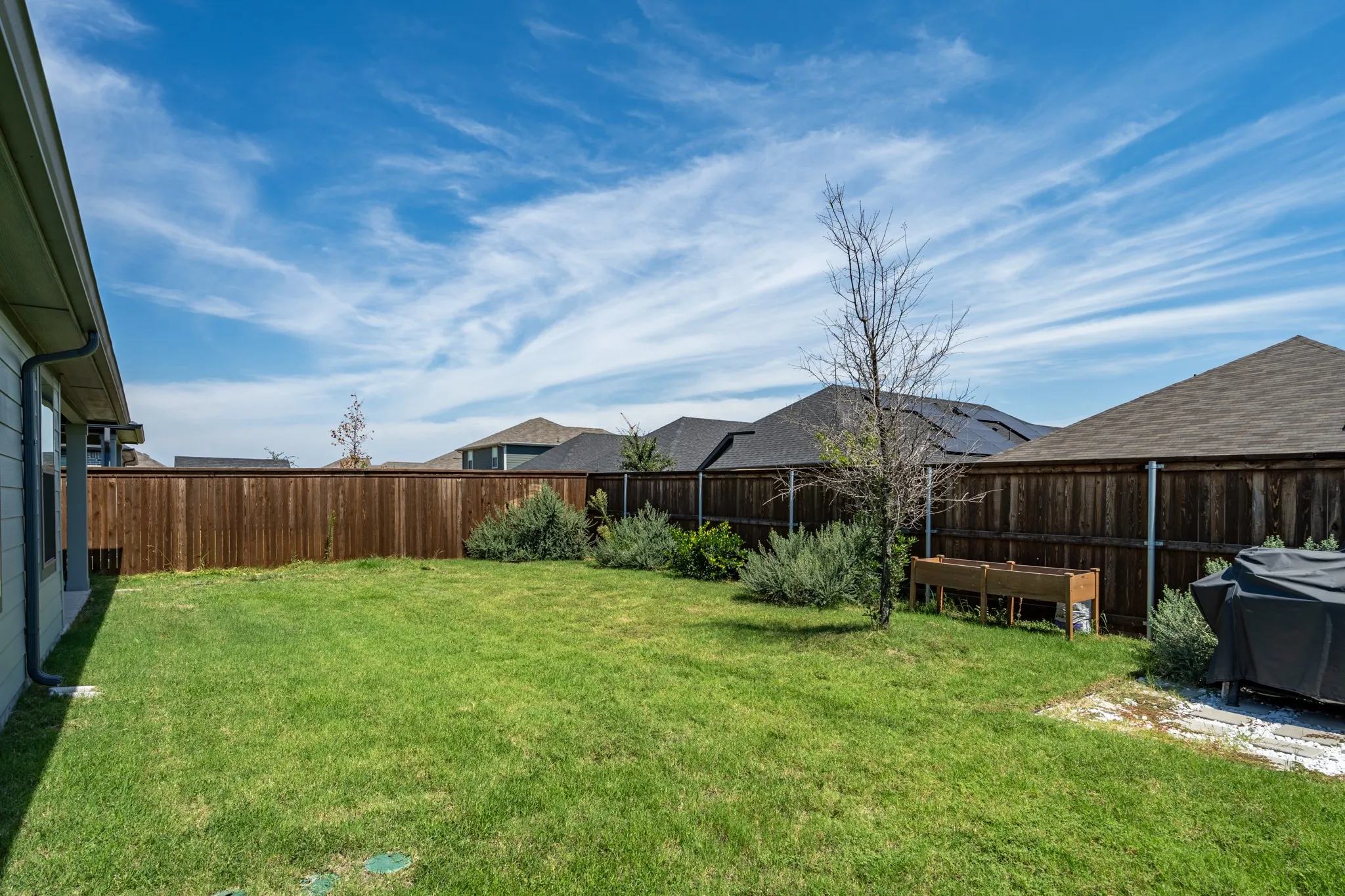 A clean view of the yard's versatile layout, complete with functional raised garden boxes, a covered grill alcove, and an airy, open-concept lawn.