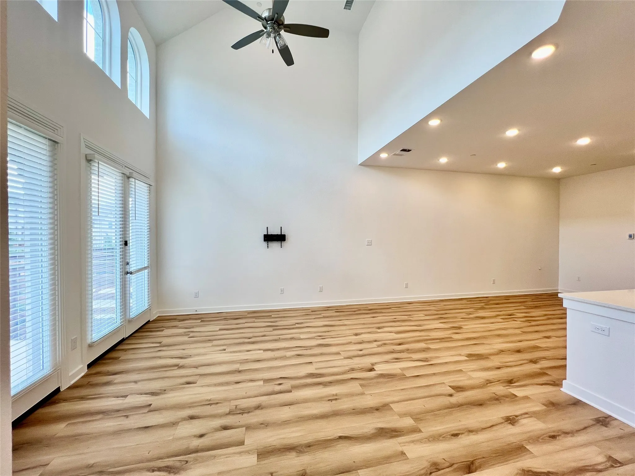 Unfurnished living room featuring plenty of natural light, light hardwood / wood-style floors, ceiling fan, and a high ceiling