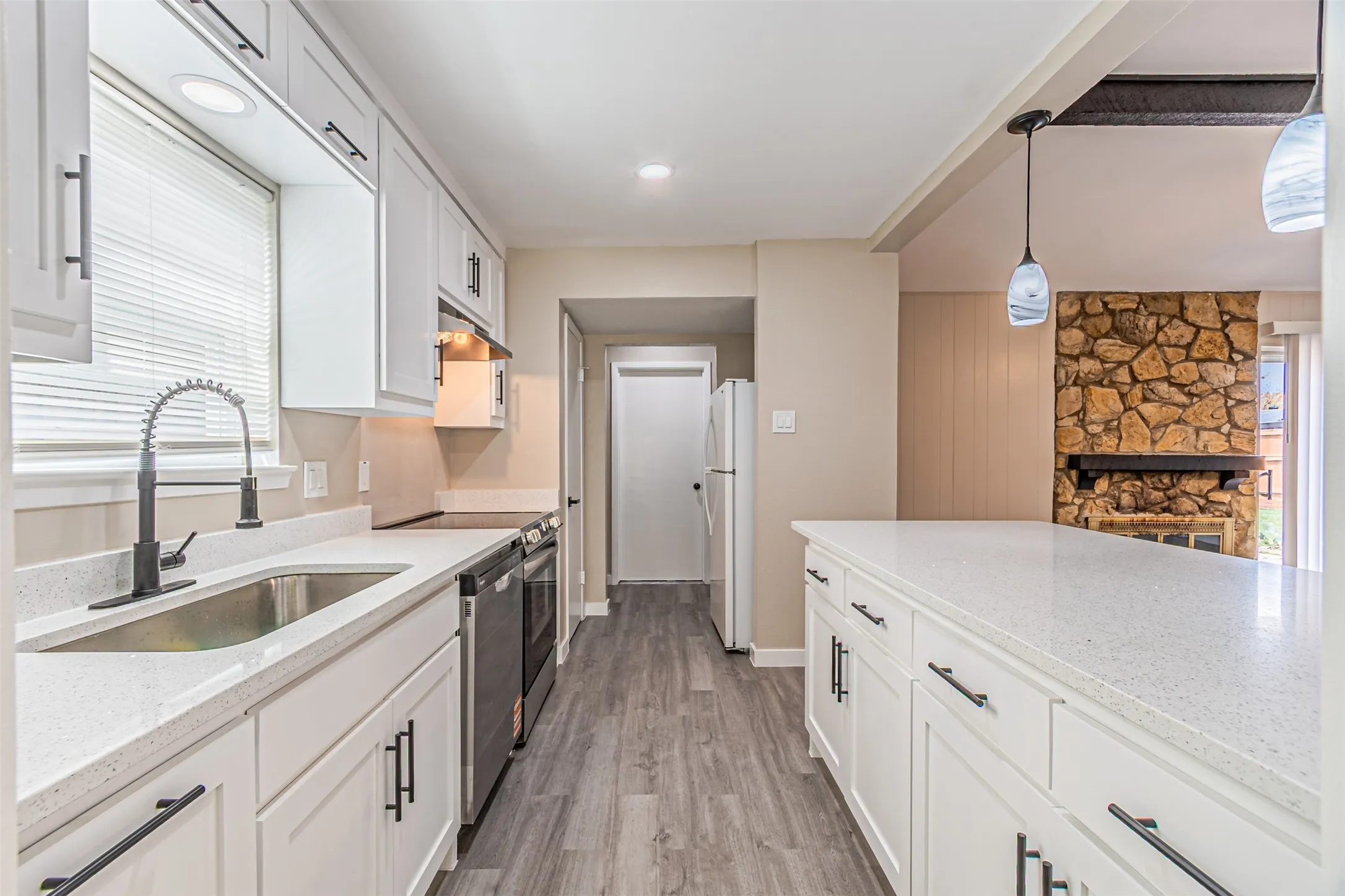 Kitchen featuring white shaker cabinetry, light-colored countertops, wood-finish flooring, and a stone-faced fireplace in the adjacent room