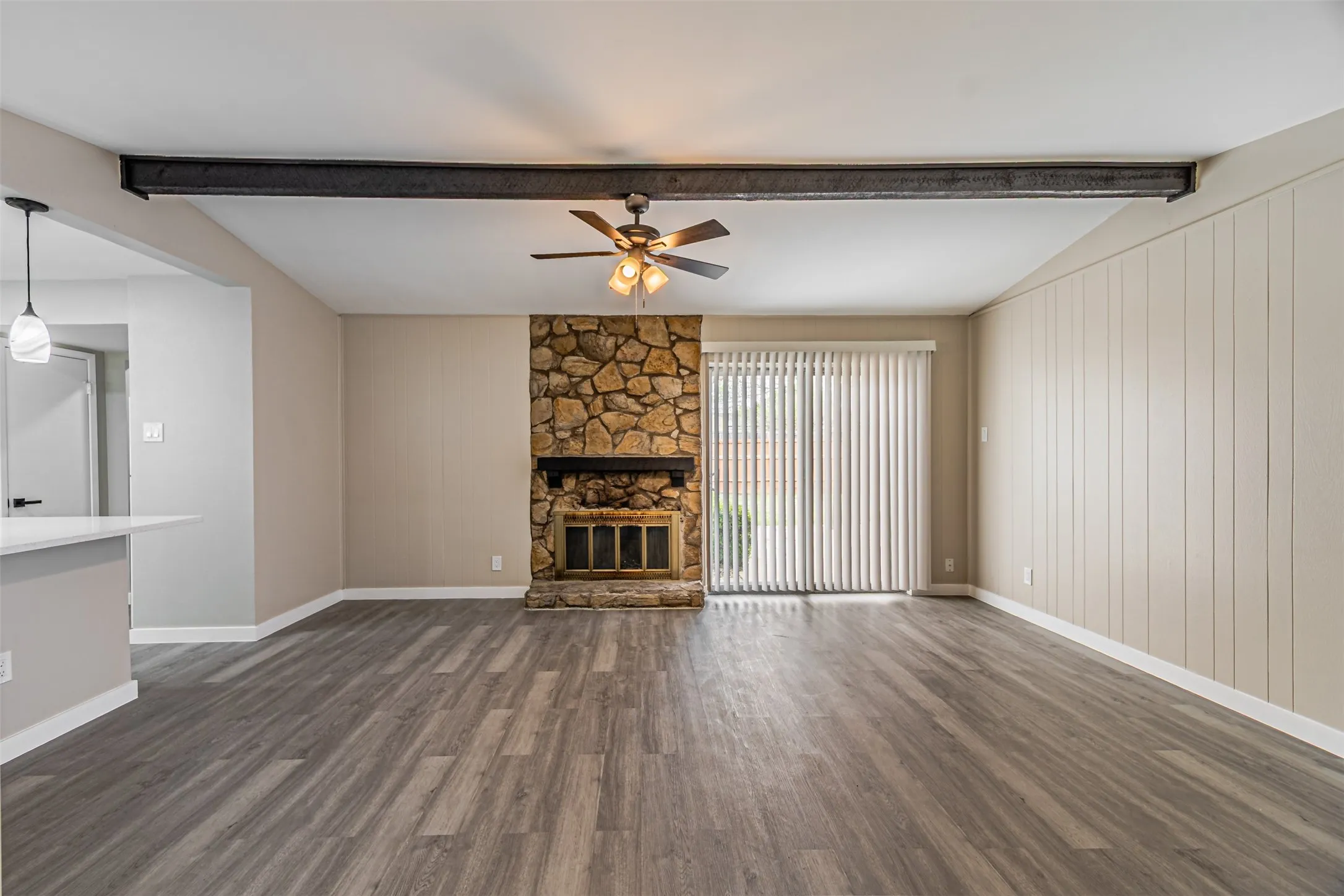 Spacious room featuring wood-finish flooring, a stone fireplace, exposed beam, and direct outdoor access via sliding glass doors