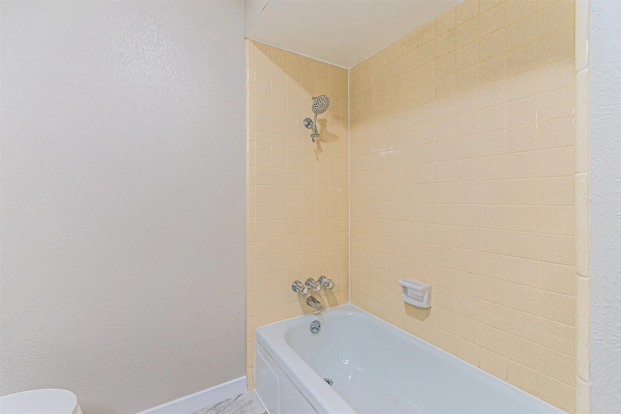 Bathtub with chrome fixtures, tiled shower surround, and a wall-mounted soap dish