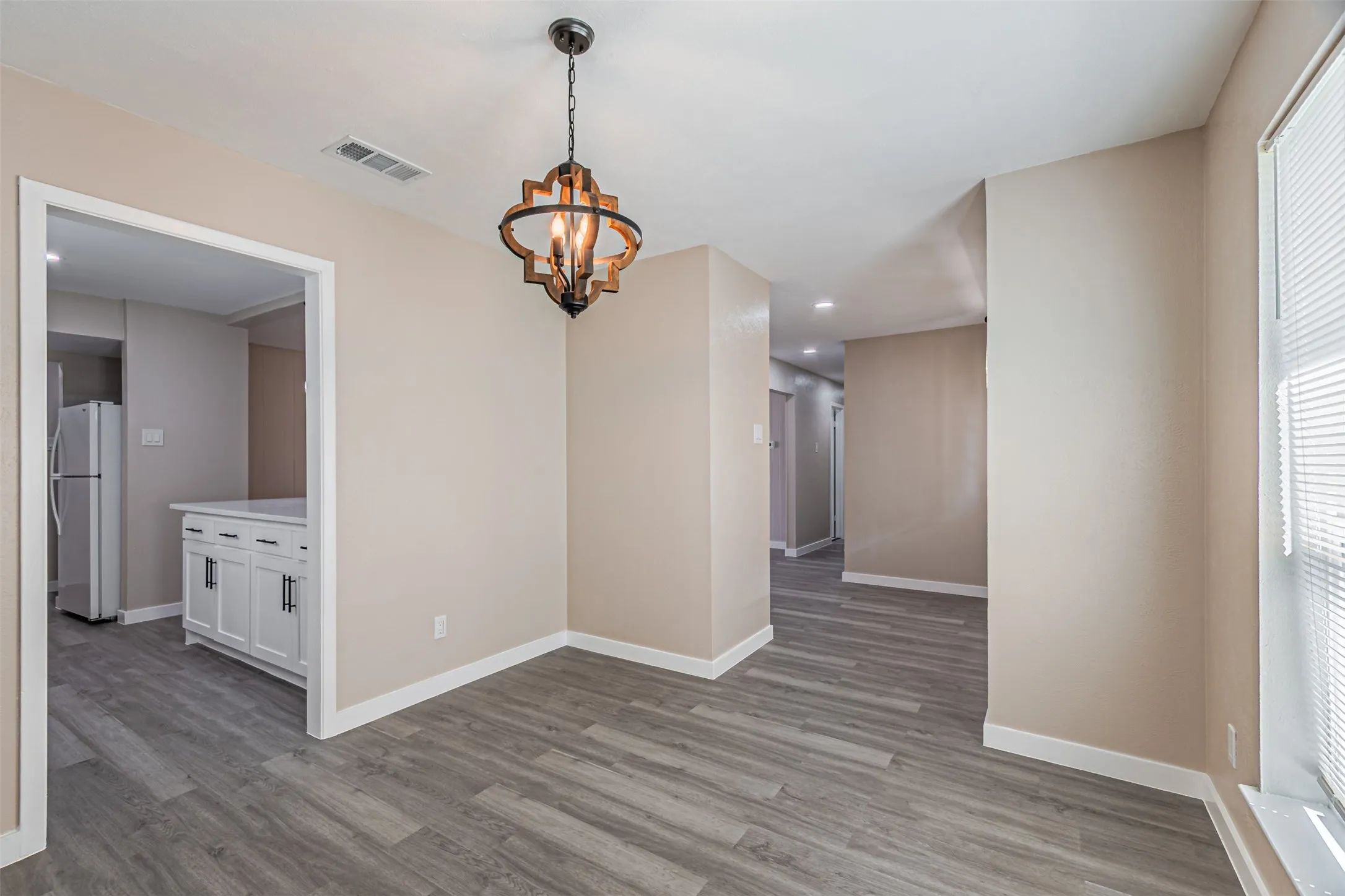 Wood-finish flooring throughout, featuring a decorative chandelier, white baseboards, and a window with horizontal blinds