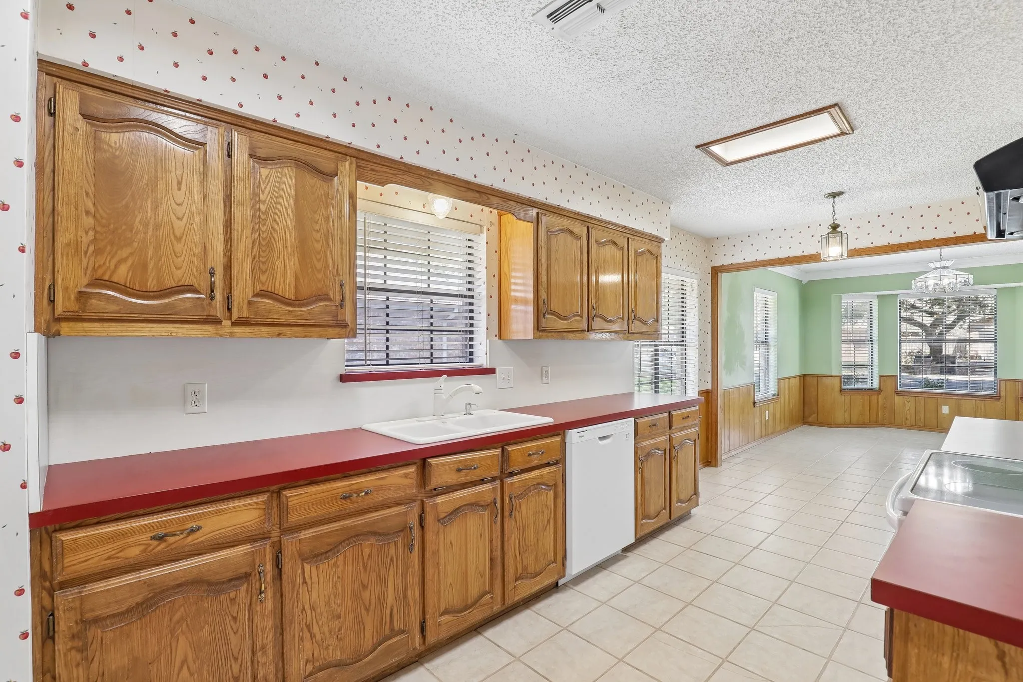 Kitchen featuring wood cabinetry, red countertops, integrated white dishwasher, and tile flooring