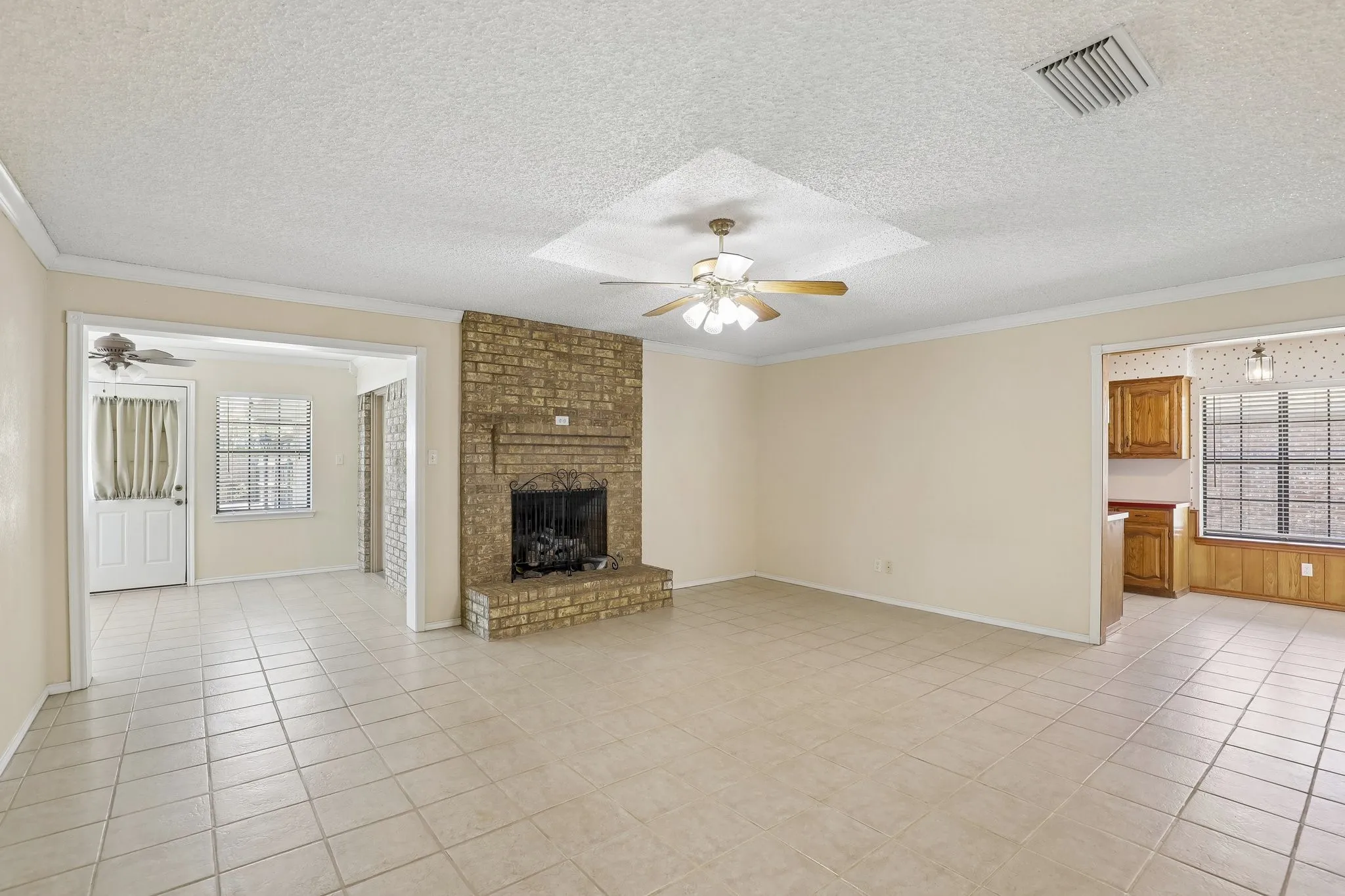 Brick-clad fireplace with a hearth, tiled flooring, ceiling fan, and an arched entryway