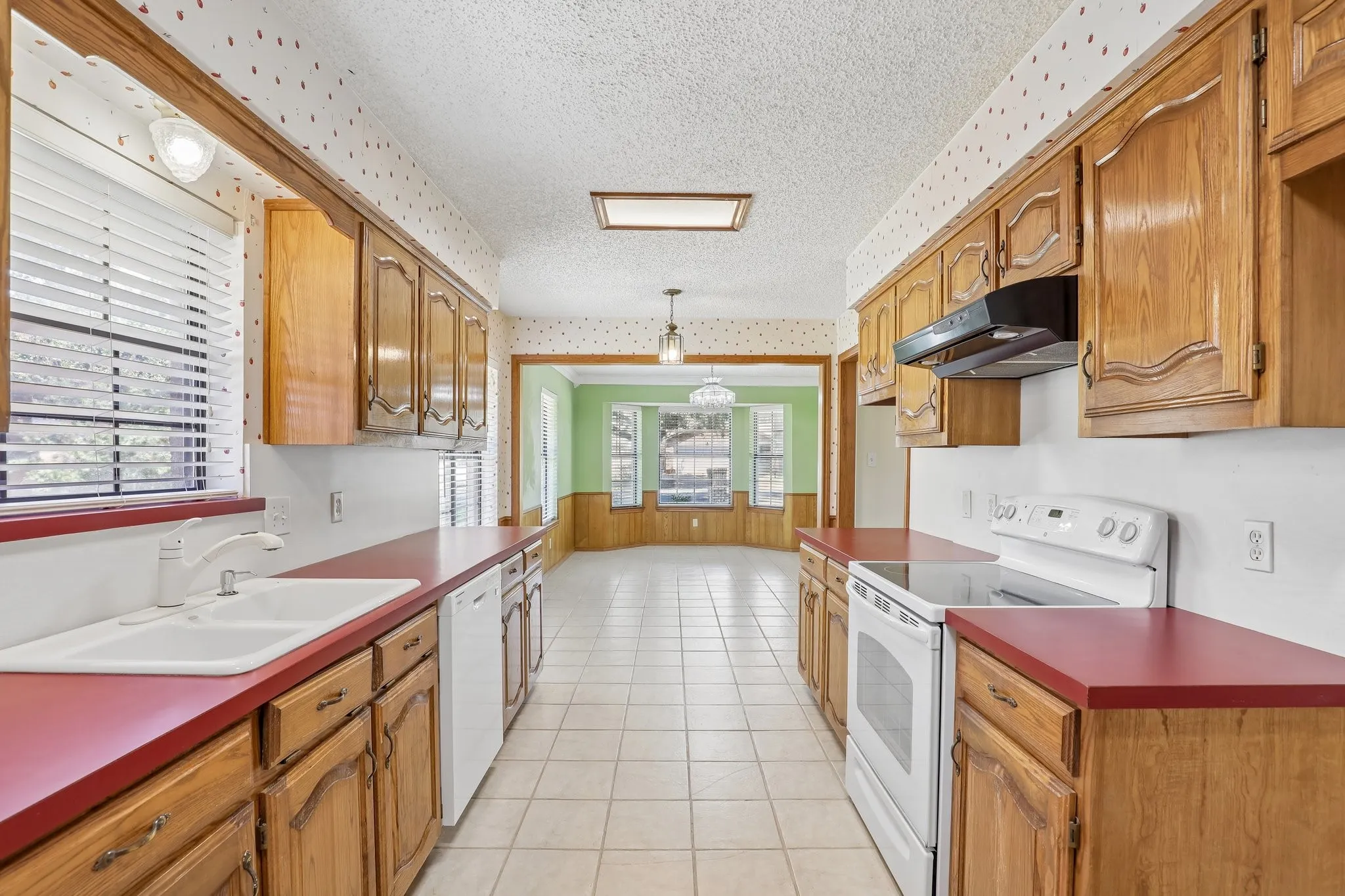 Galley-style kitchen featuring wood cabinetry, red countertops, and white tile flooring