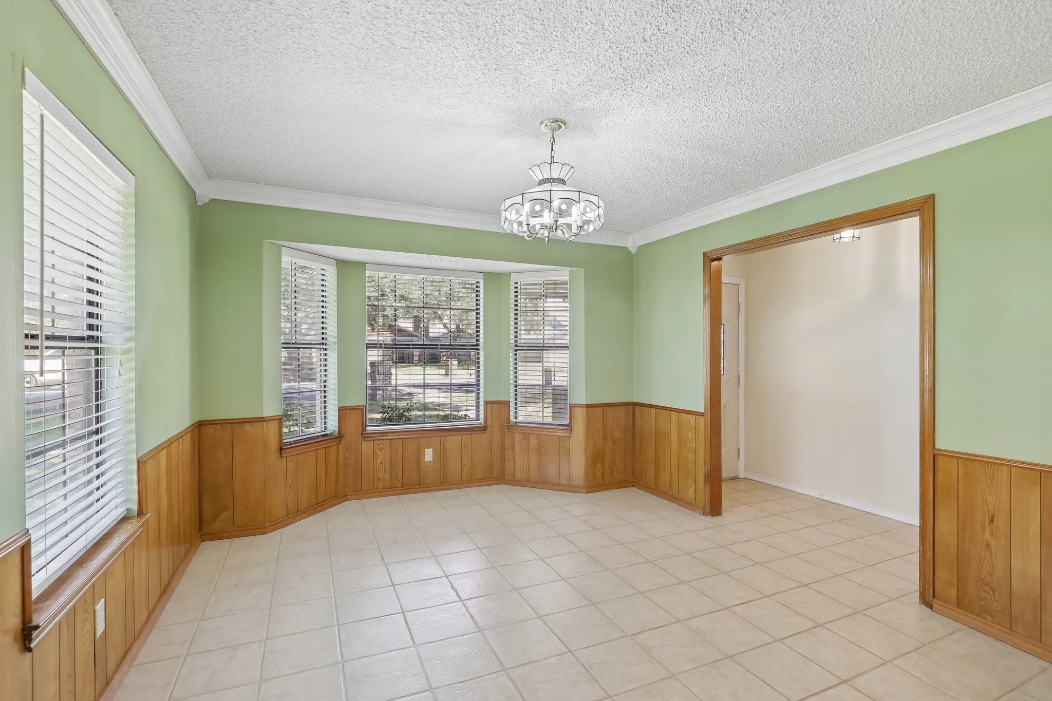 Tile flooring, bay windows, wood paneling, crown molding, and a decorative ceiling fixture