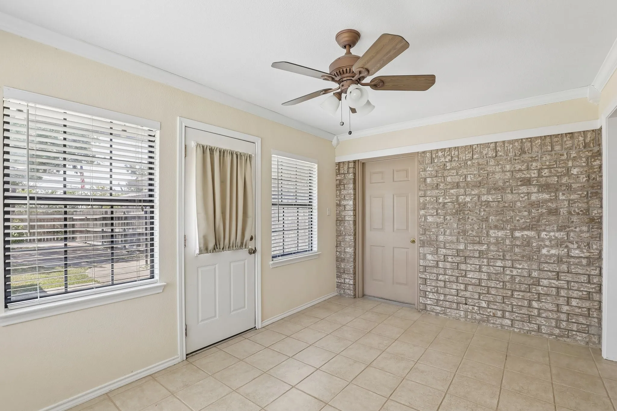 Tiled flooring with an exposed brick accent wall, white trim, and a ceiling fan with integrated lighting