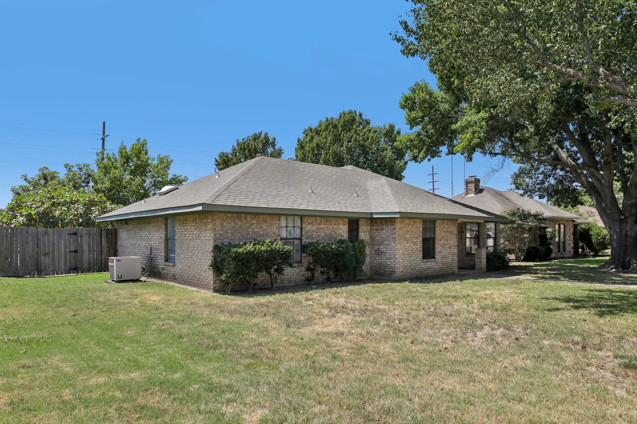 Brick exterior with a shingled roof, mature landscaping, and a fenced rear perimeter