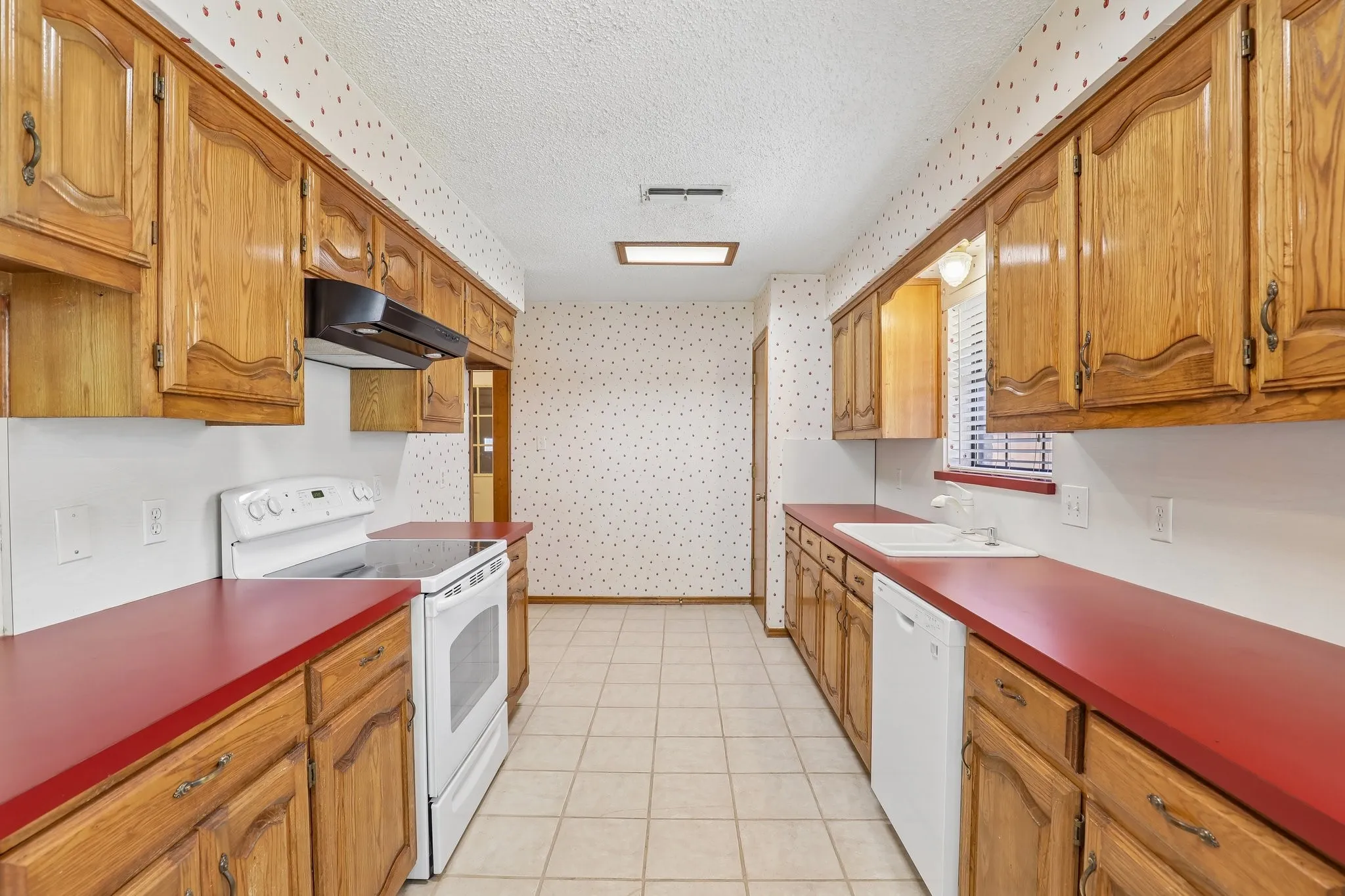 Galley kitchen with wood cabinetry, red countertops, tile flooring, electric range, and ventahood