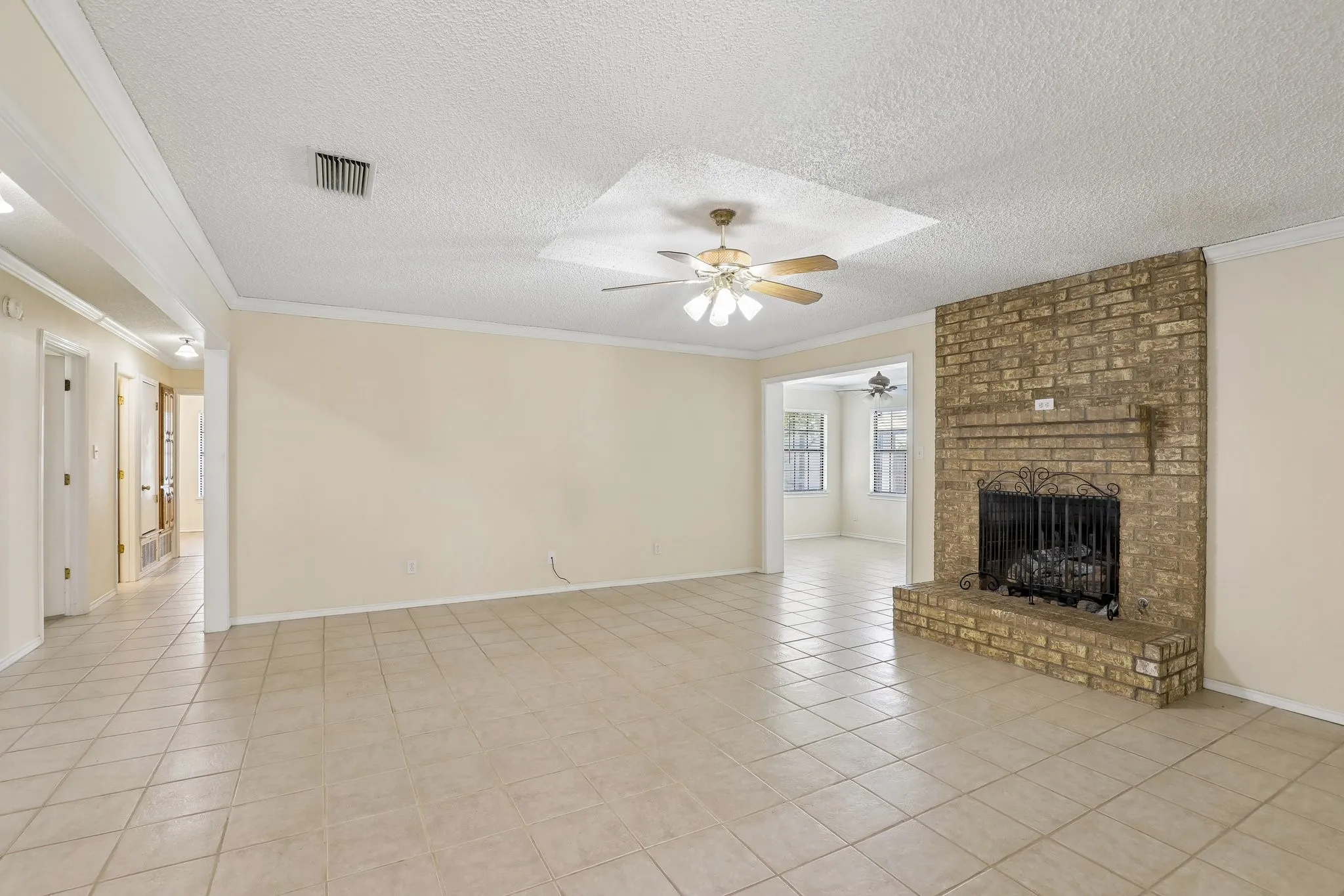 Spacious room featuring tiled flooring, a brick fireplace, crown molding, and a ceiling fan