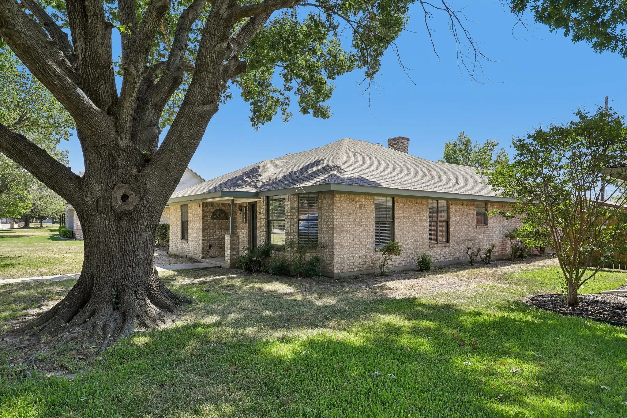 Brick exterior with a shingled roof, mature landscaping, and a fenced rear perimeter