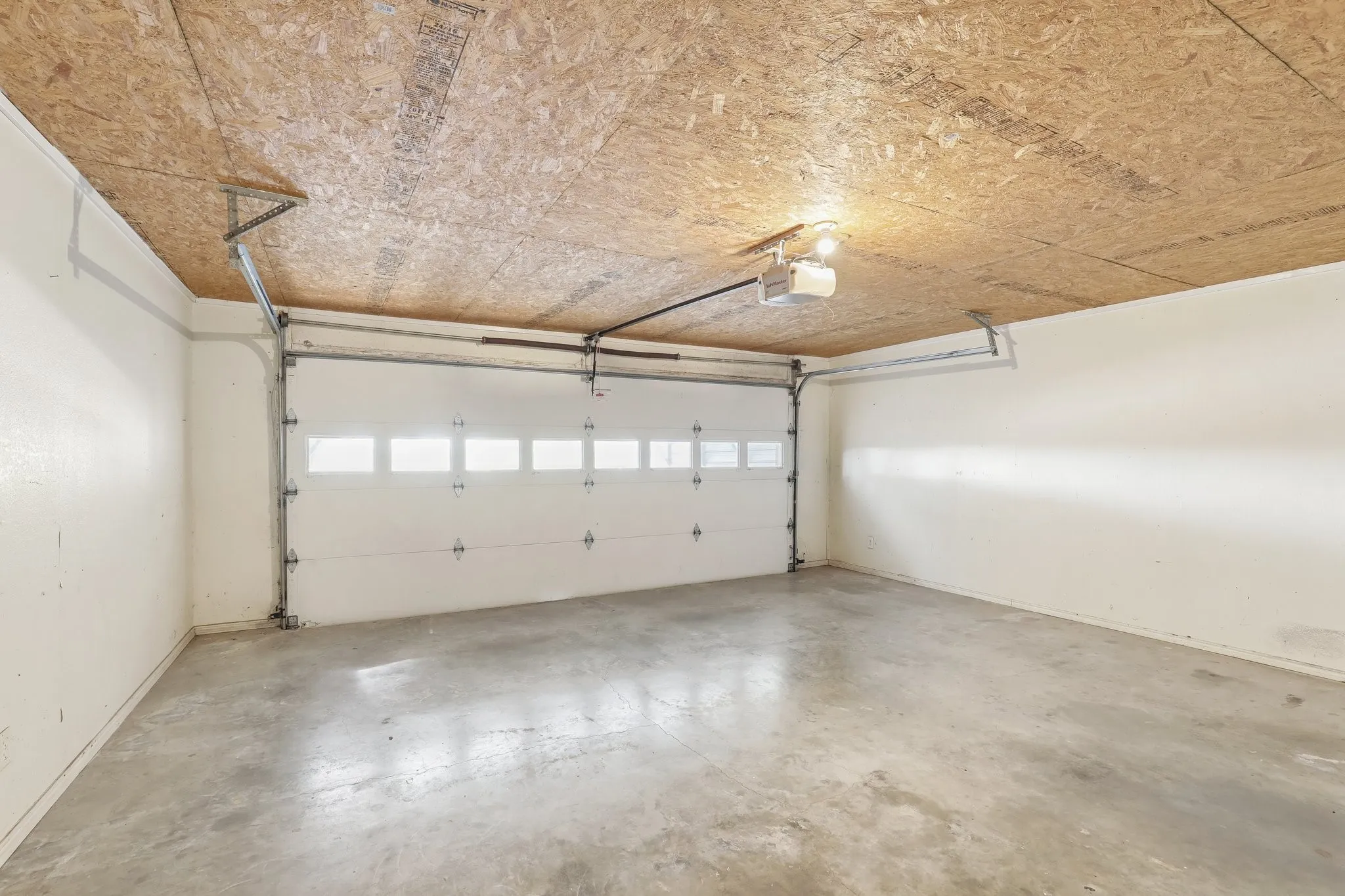 Spacious two car garage featuring a concrete floor, overhead lighting, and an automatic garage door opener
