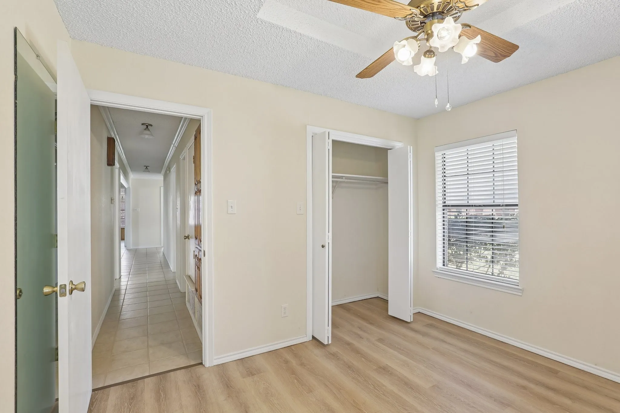Wood-finish flooring, built-in closet with bi-fold doors, window with blinds, ceiling fan with light fixture, and textured ceiling