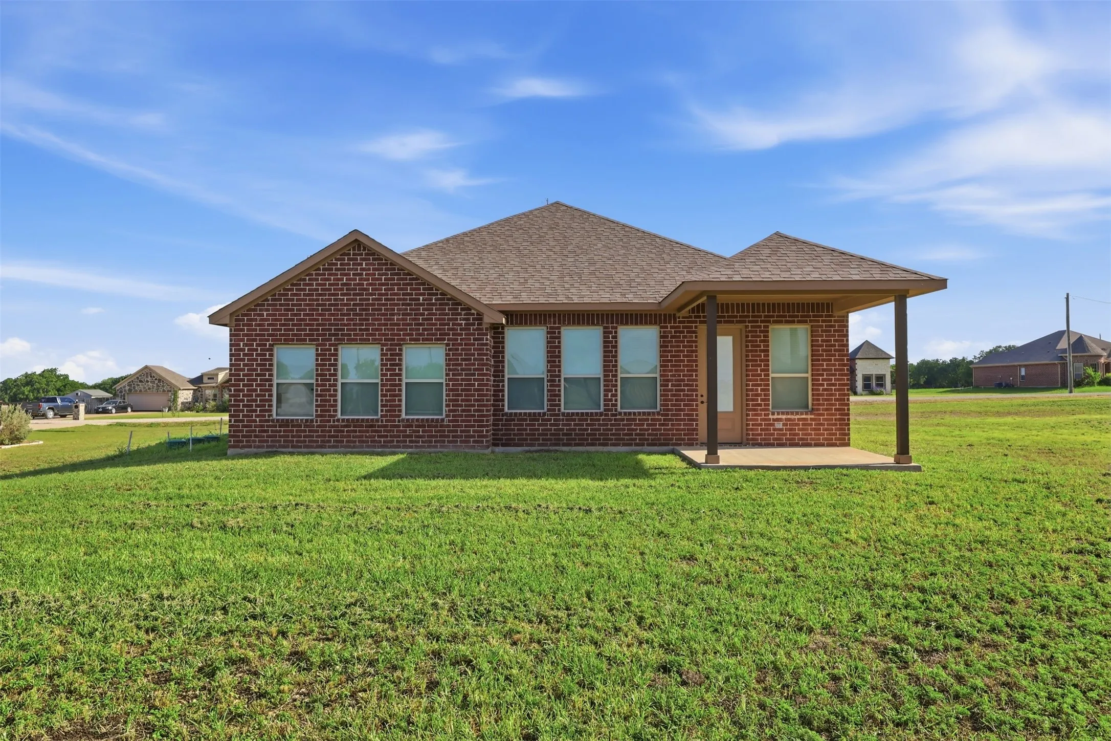 Brick exterior with a covered patio, multiple windows, and a shingle roof