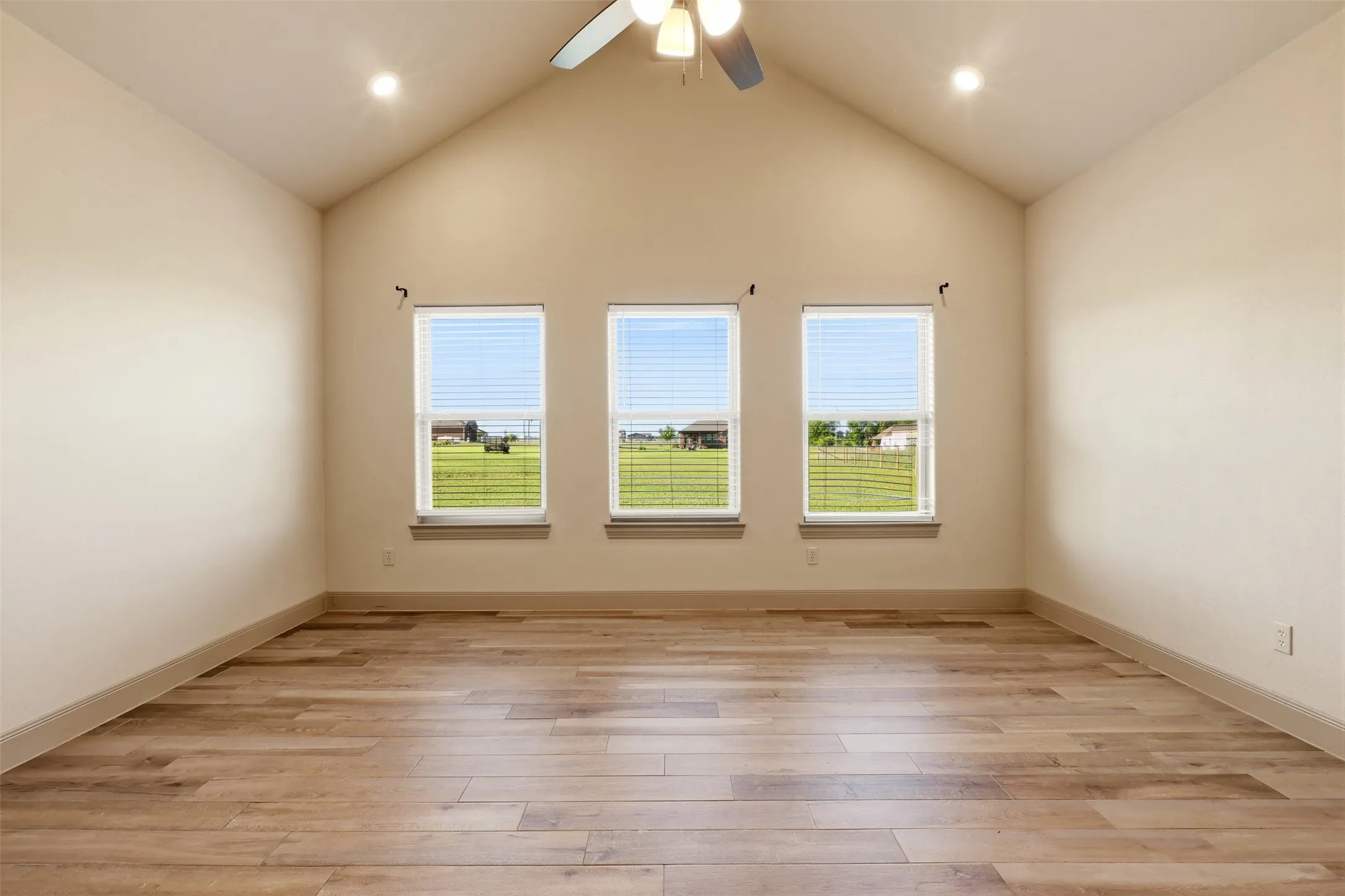 Vaulted ceiling, wood-finish flooring, three windows with blinds, ceiling fan, and recessed lighting