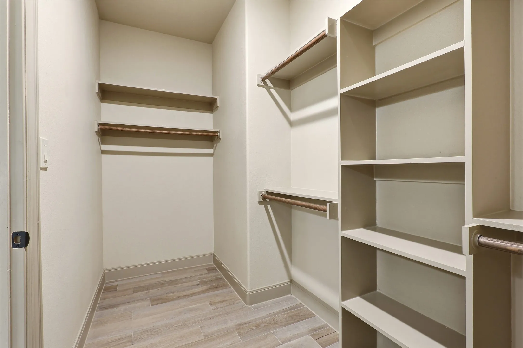 Custom closet system with built-in shelving, multiple hanging rods, and wood-finish flooring