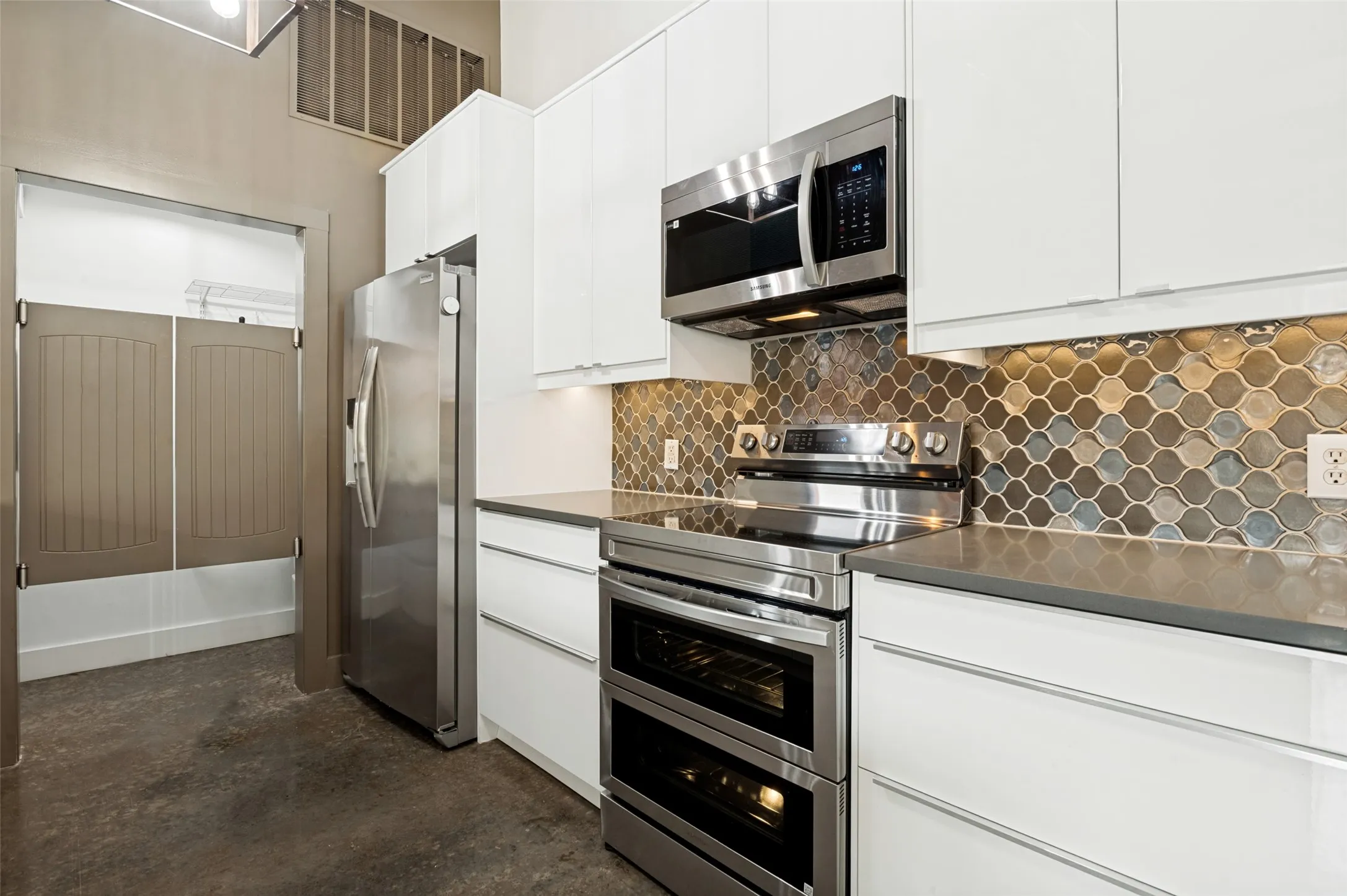 Contemporary kitchen featuring white cabinetry, stainless steel appliances, a mosaic tile backsplash, and a dark-toned countertop