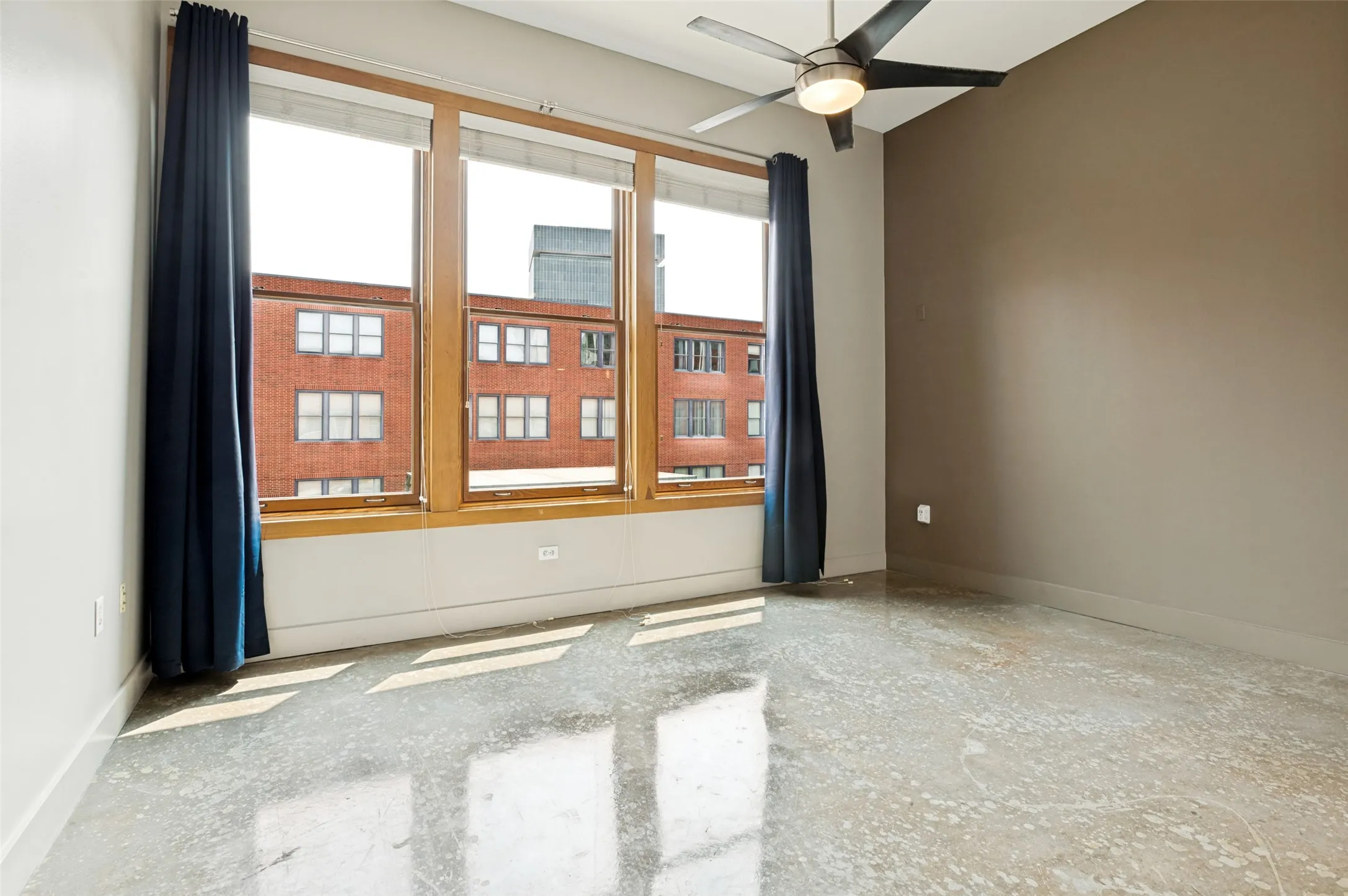 Primary suite with polished concrete flooring, floor-to-ceiling windows with wood frames, and a ceiling fan with integrated lighting