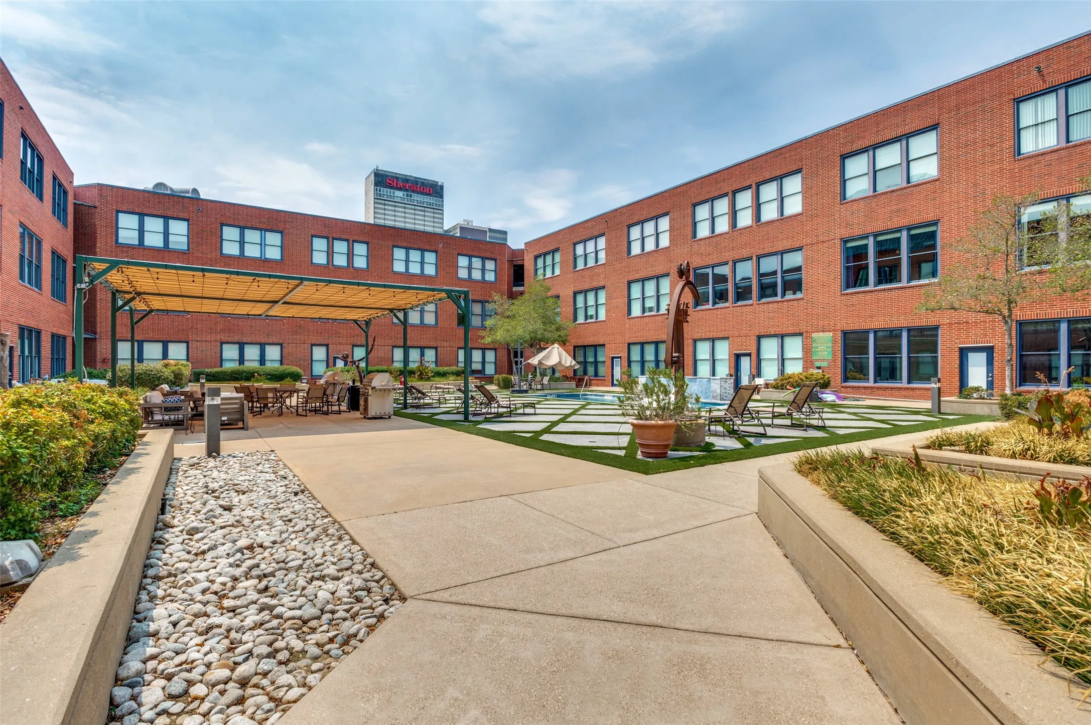 Courtyard featuring a pergola-covered patio, concrete pathways, manicured landscaping, and a central water feature