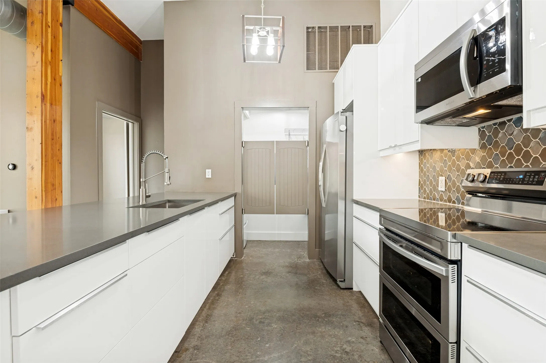 Contemporary kitchen featuring white cabinetry, stainless steel appliances, grey countertops, a patterned backsplash, and concrete flooring