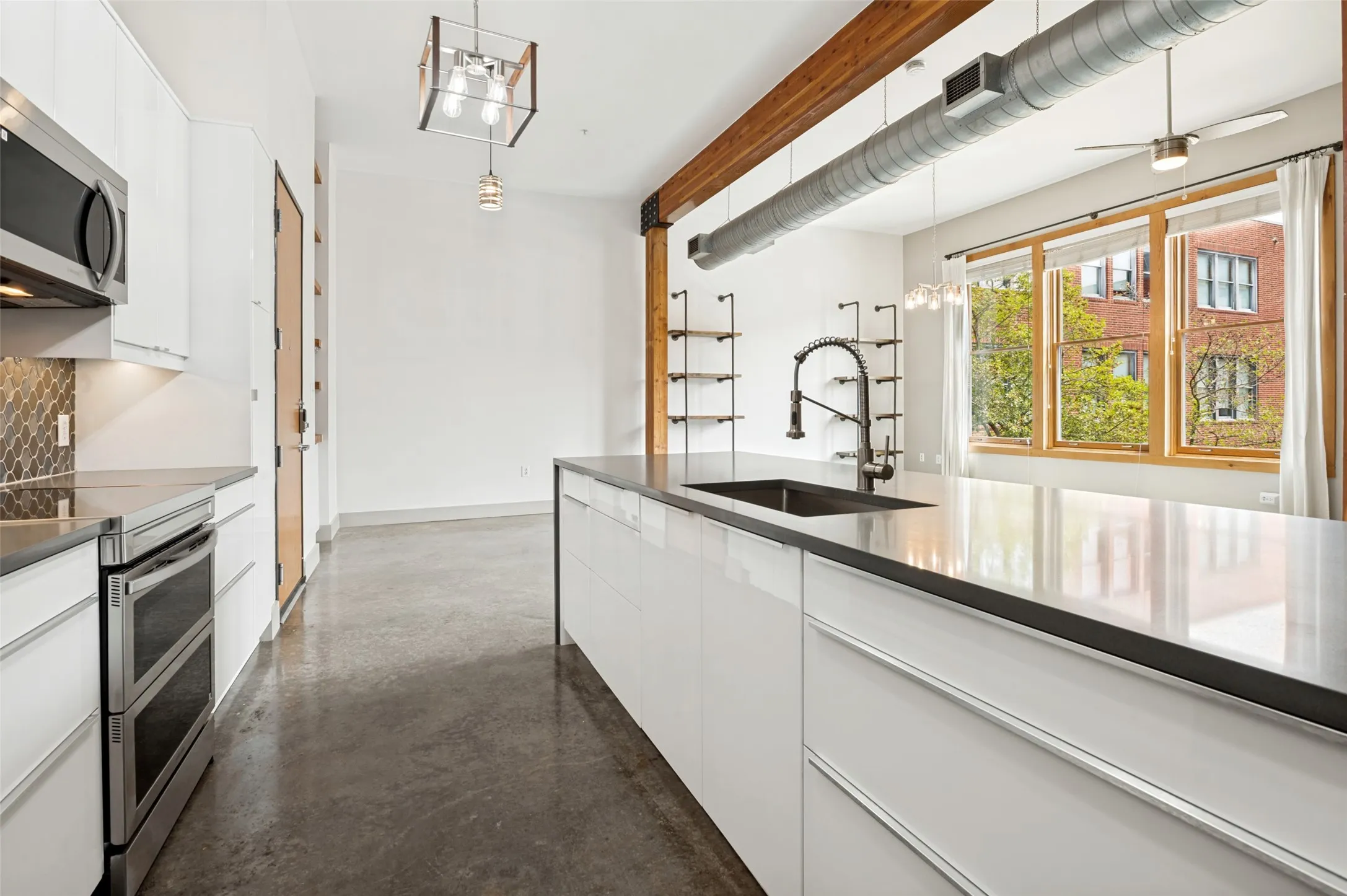Modern kitchen featuring a stainless steel double oven, sleek white cabinetry, a large kitchen island with an undermount sink, and polished concrete flooring