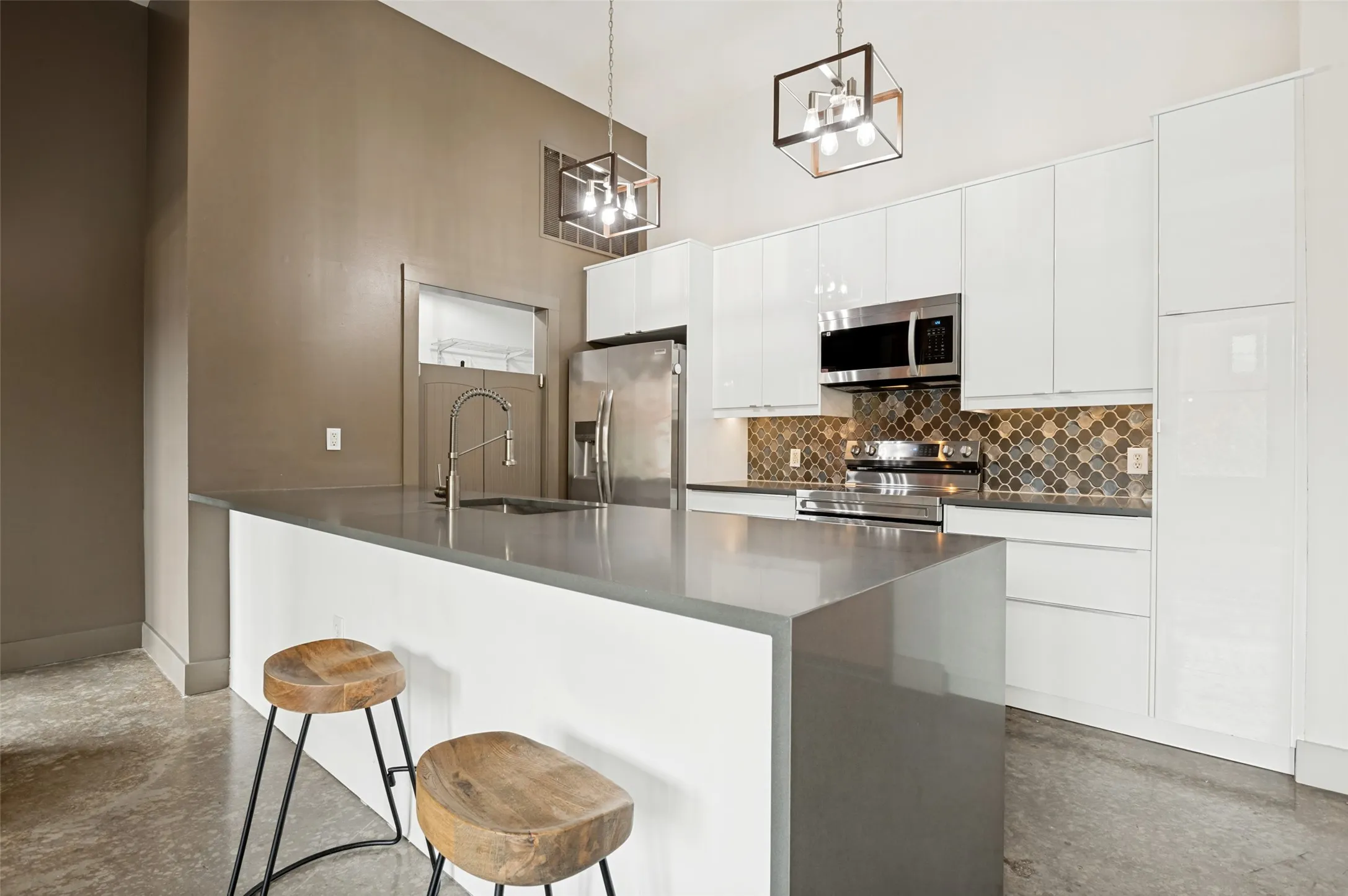 Kitchen featuring a waterfall island, integrated sink, stainless steel appliances, white flat-panel cabinetry, and a mosaic tile backsplash
